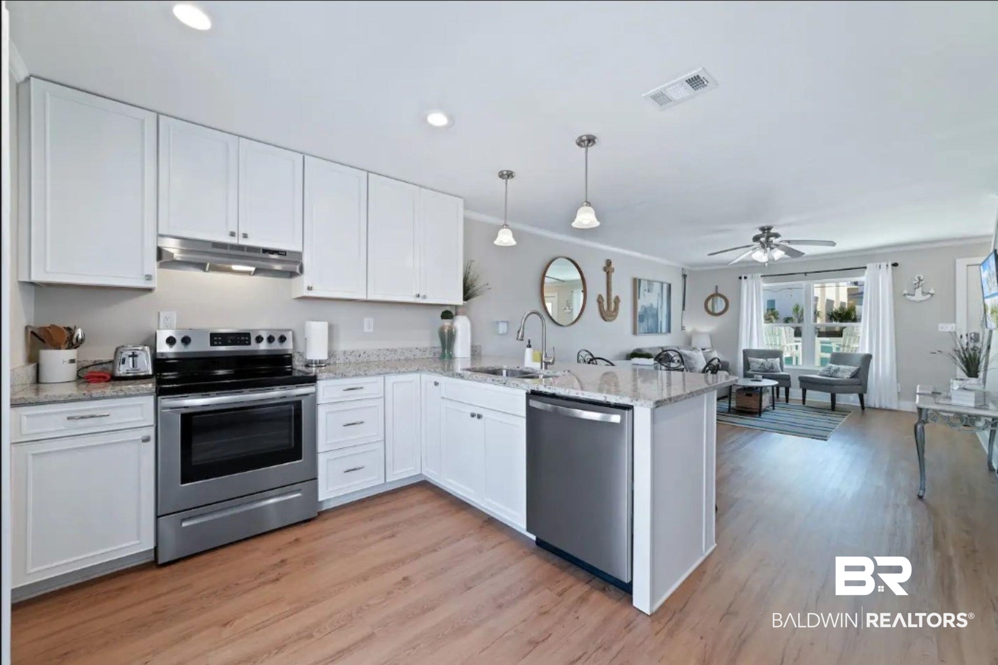 Bright kitchen with white cabinets, granite island, stainless steel appliances, and an adjoining furnished living area.
