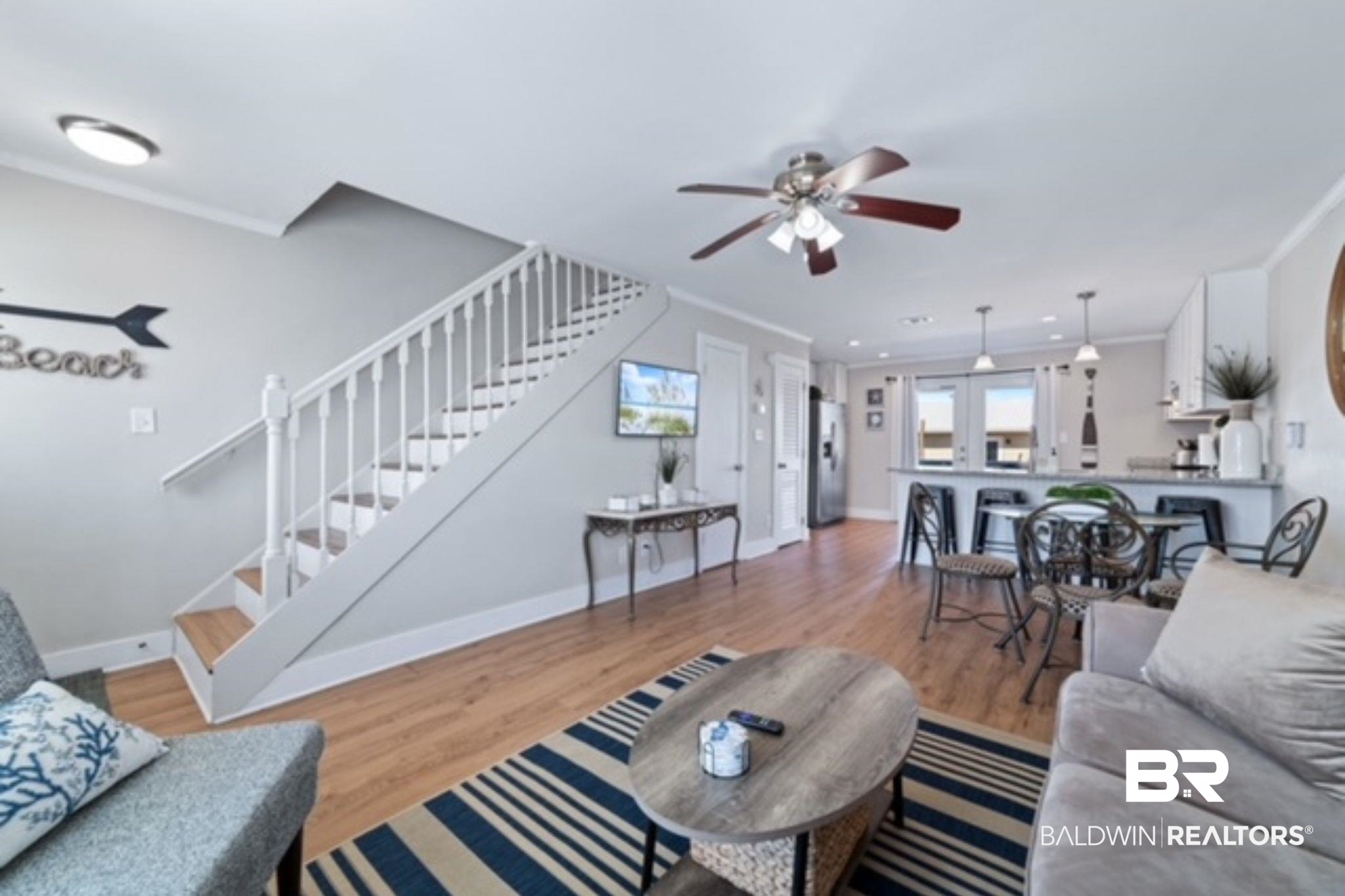 Furnished living room opening to a kitchen and dining area, with a staircase and striped rug.