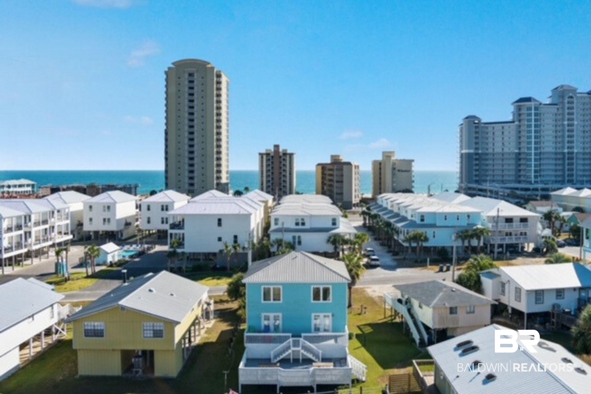 Coastal homes near the Gulf, with a blue house in front and condominium towers along the shore.