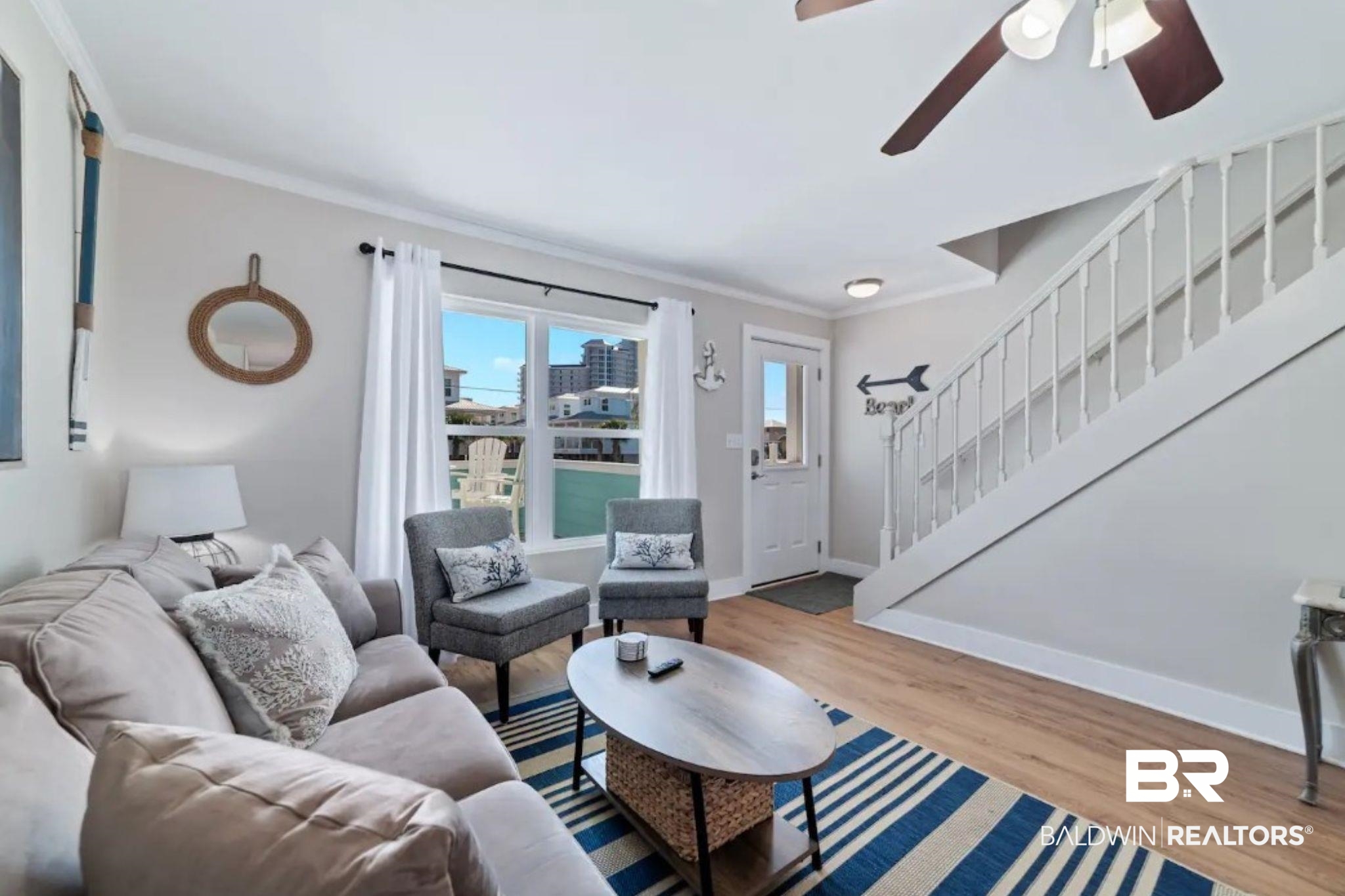 Living room with a striped rug, gray seating, staircase, and windows overlooking a pool.