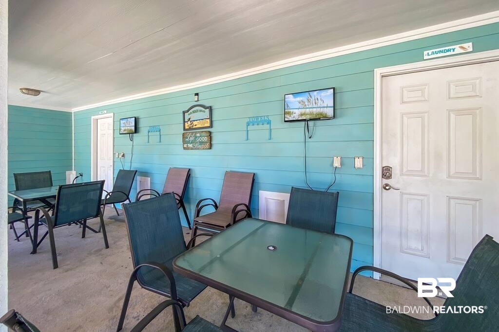 Covered patio with turquoise siding, a glass-top table, and dark chairs.
