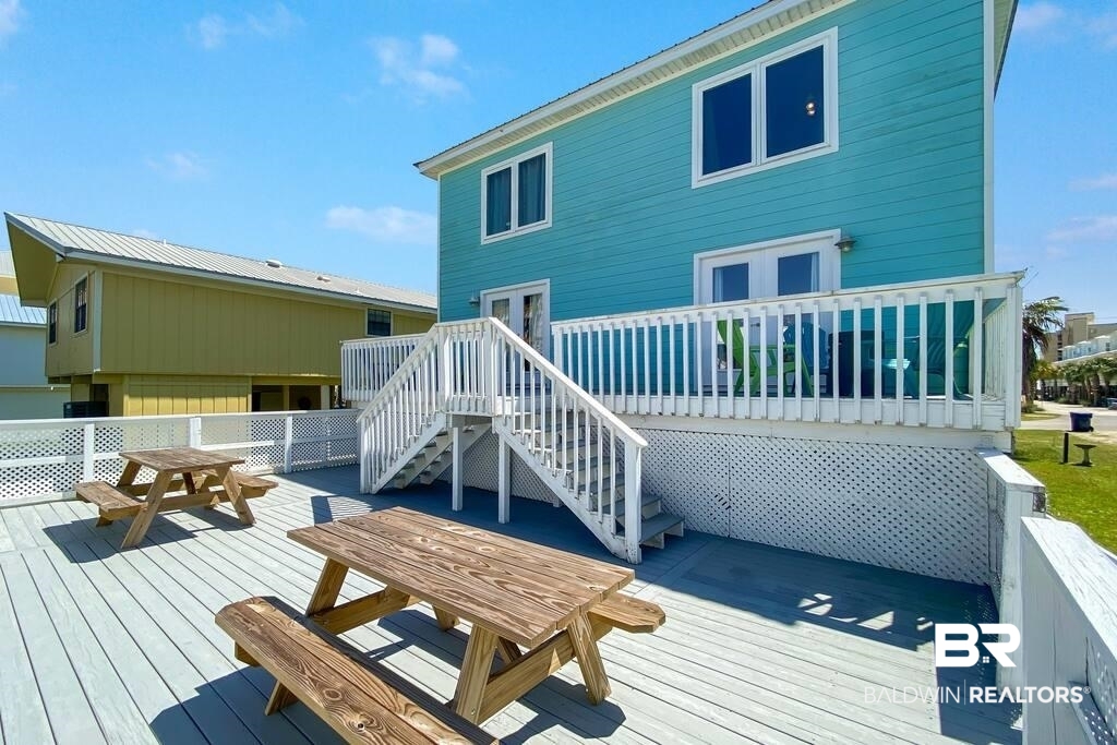 Turquoise coastal house with an elevated white deck and stairs above a spacious picnic-table patio.