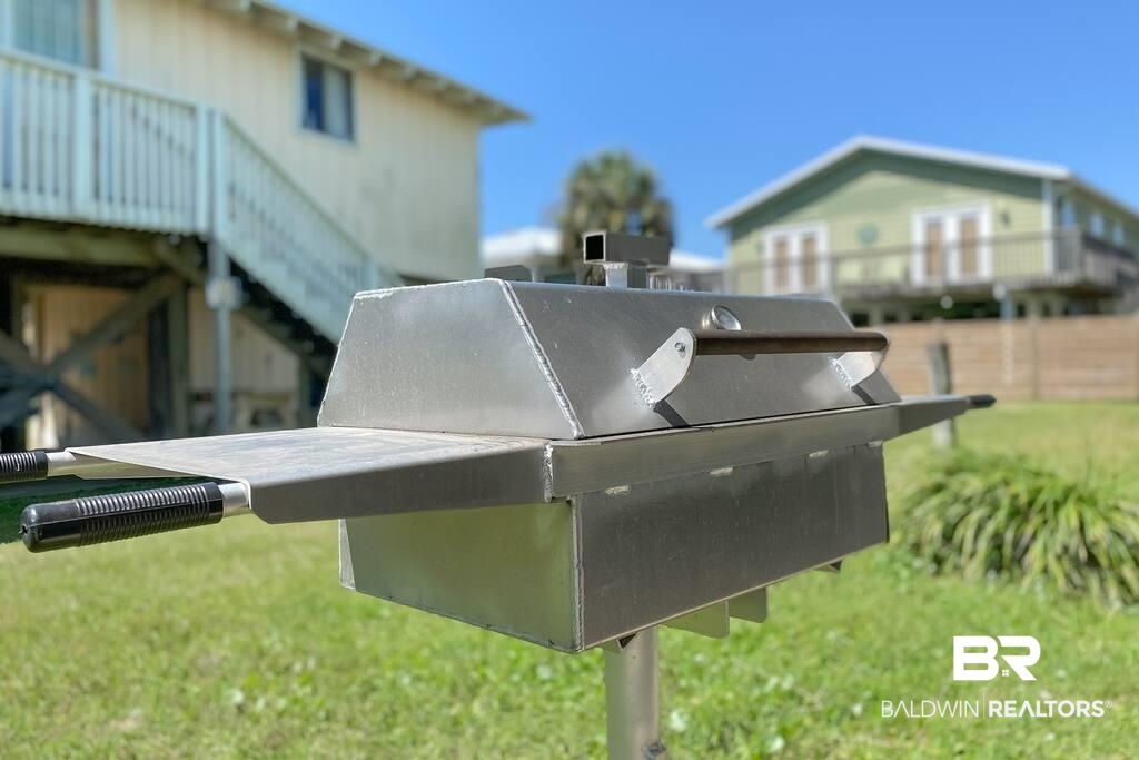 Stainless steel outdoor grill in a grassy yard between elevated beach houses.
