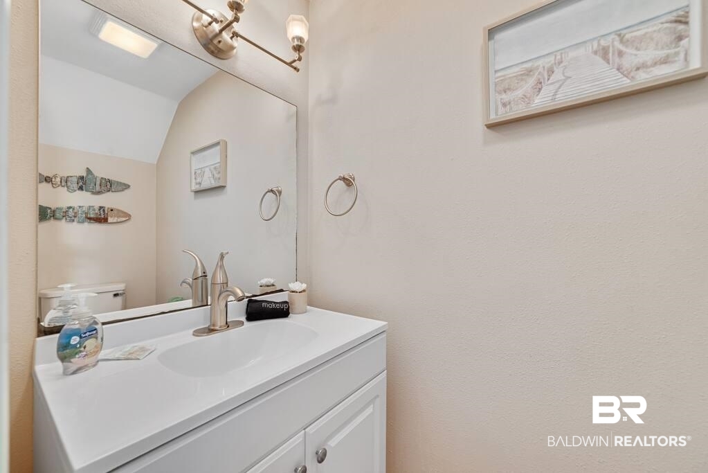 Bathroom vanity with a white sink, bronze faucet, large mirror, and coastal artwork.