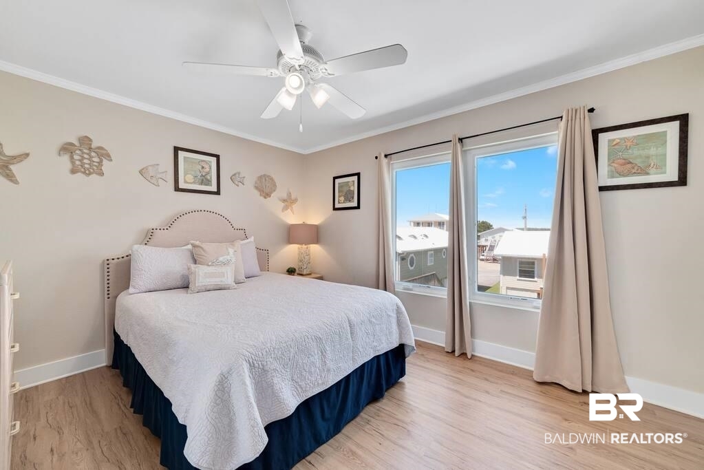 Bedroom with a white quilted bed, ceiling fan, coastal wall decor, and windows overlooking neighboring homes.