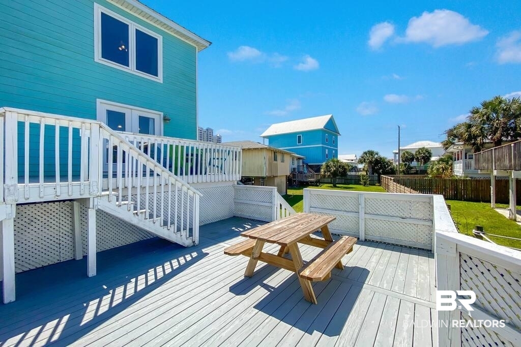Raised deck with a wooden picnic table beside a turquoise home and fenced grassy yard.