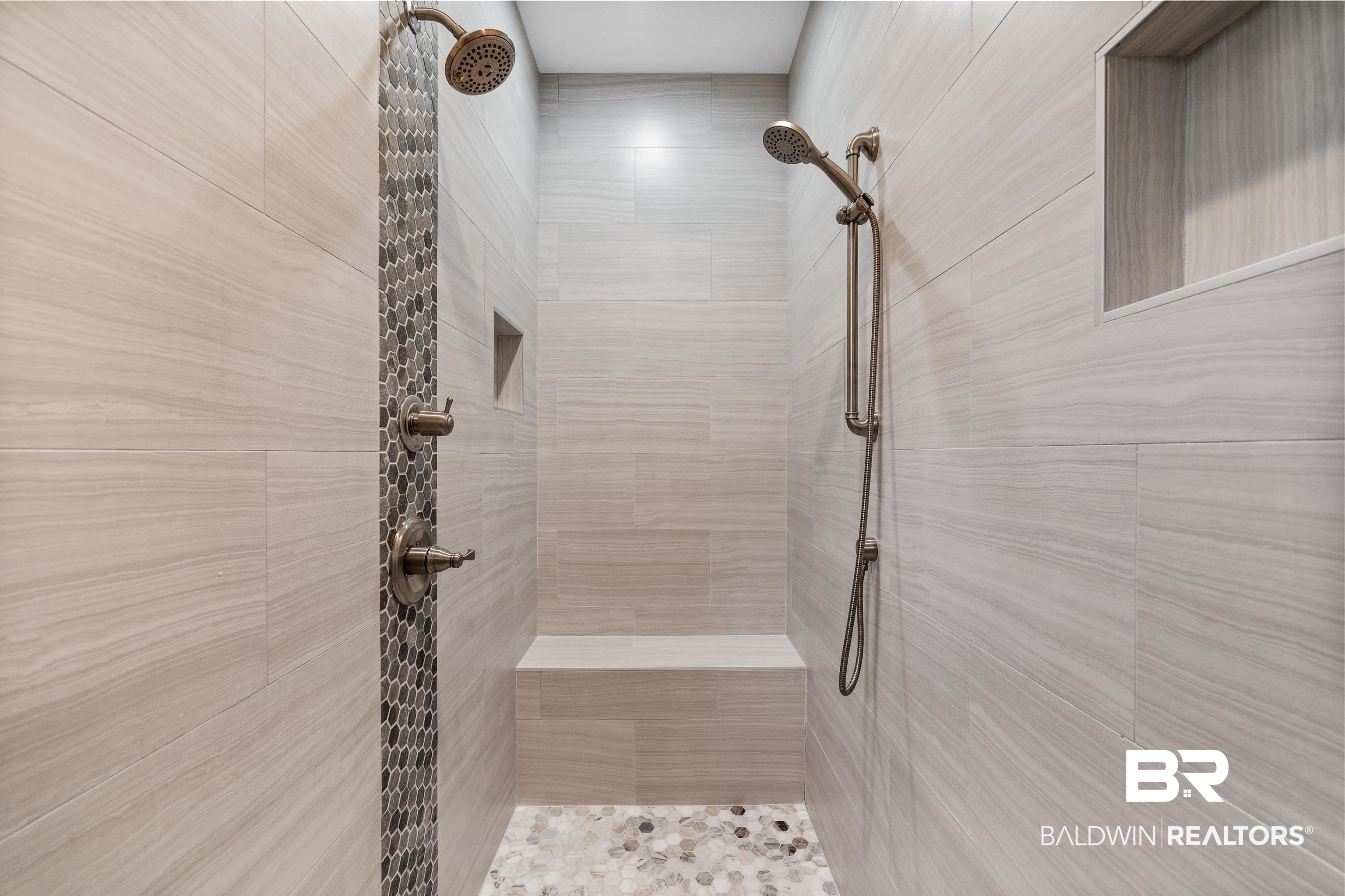 Walk-in shower with a tiled bench, dark hexagonal accent strip, and bronze fixtures.