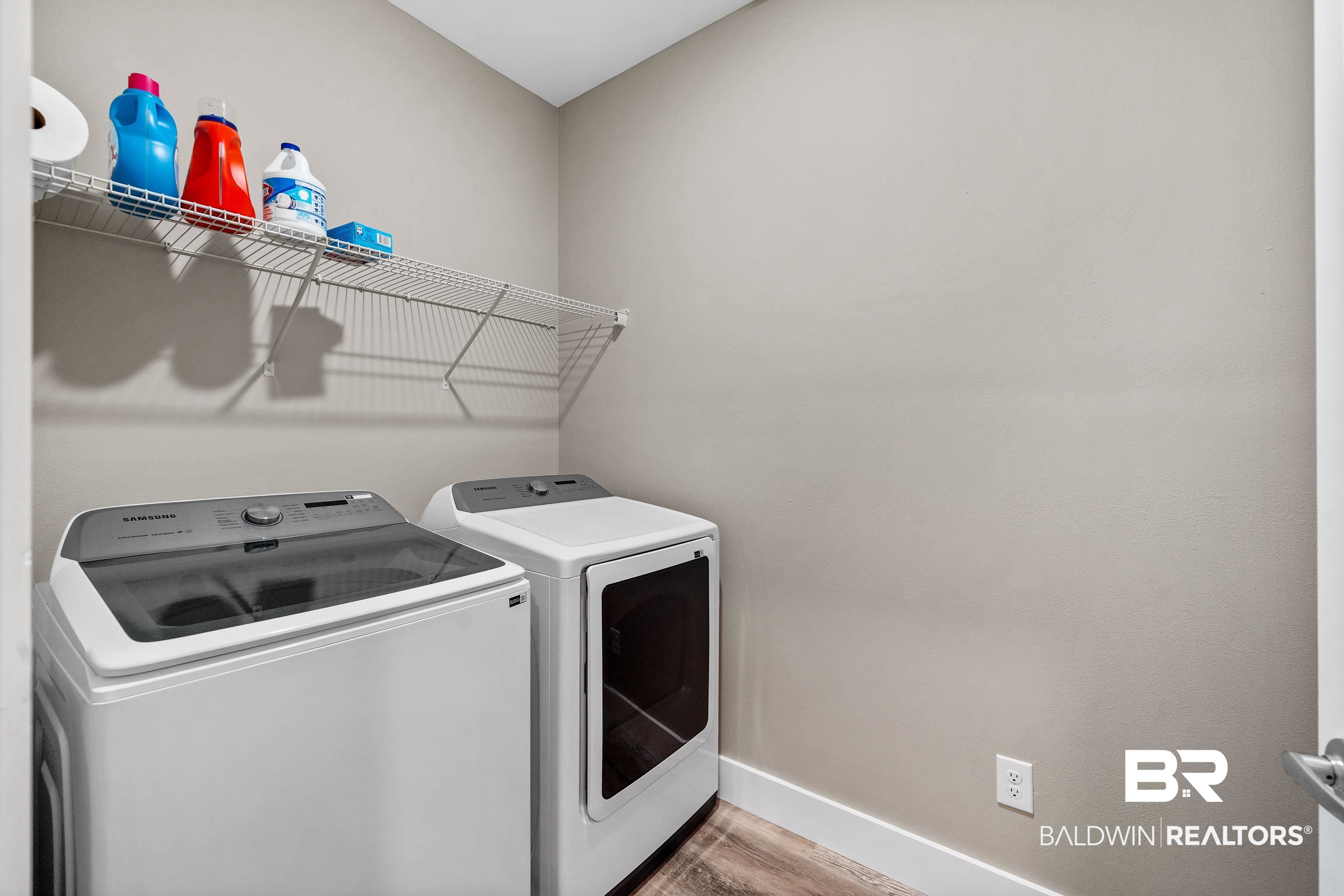 Laundry room with Samsung washer and dryer beneath a wire shelf of laundry supplies.