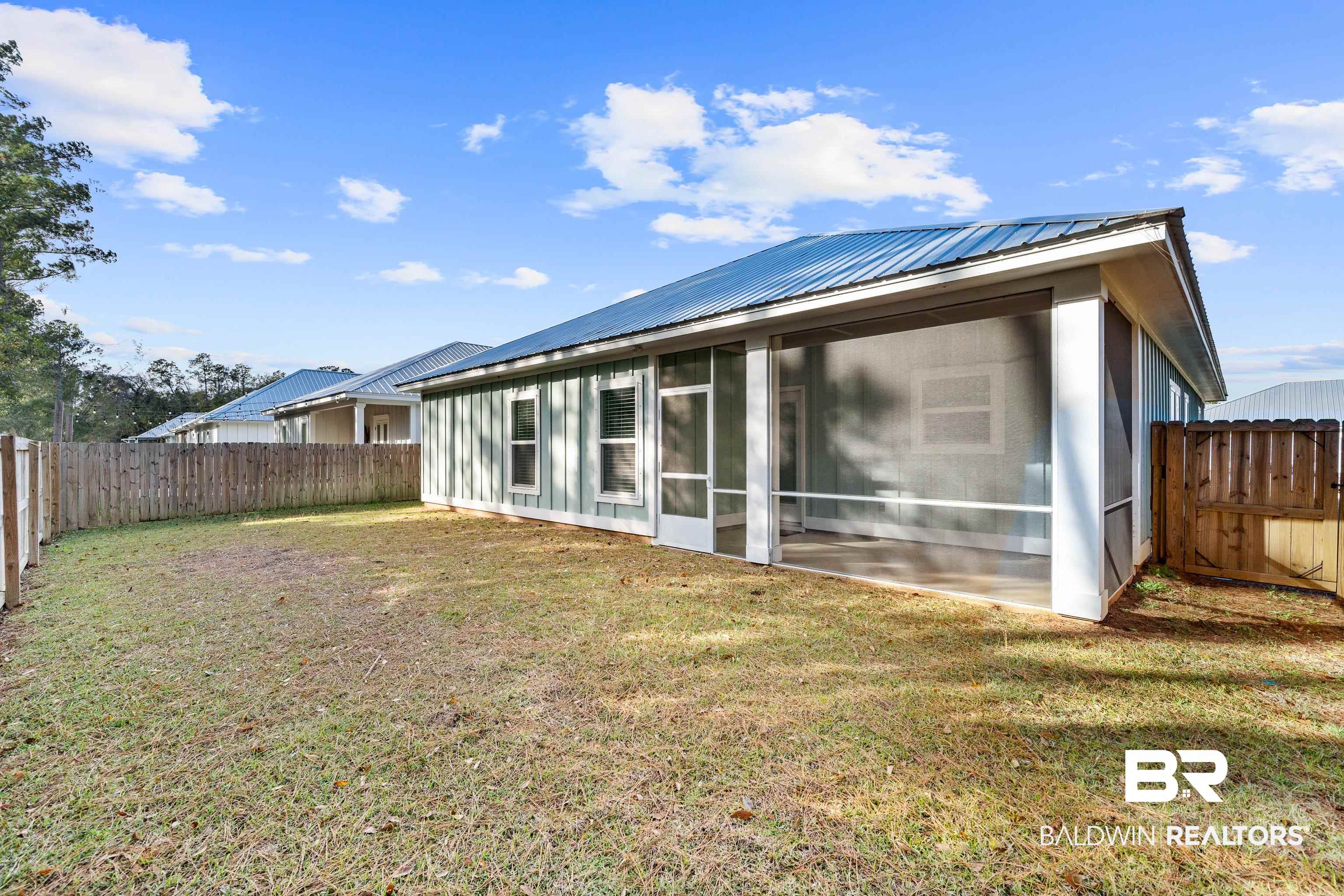 Home’s rear exterior with a large screened porch, metal roof, and fenced yard.
