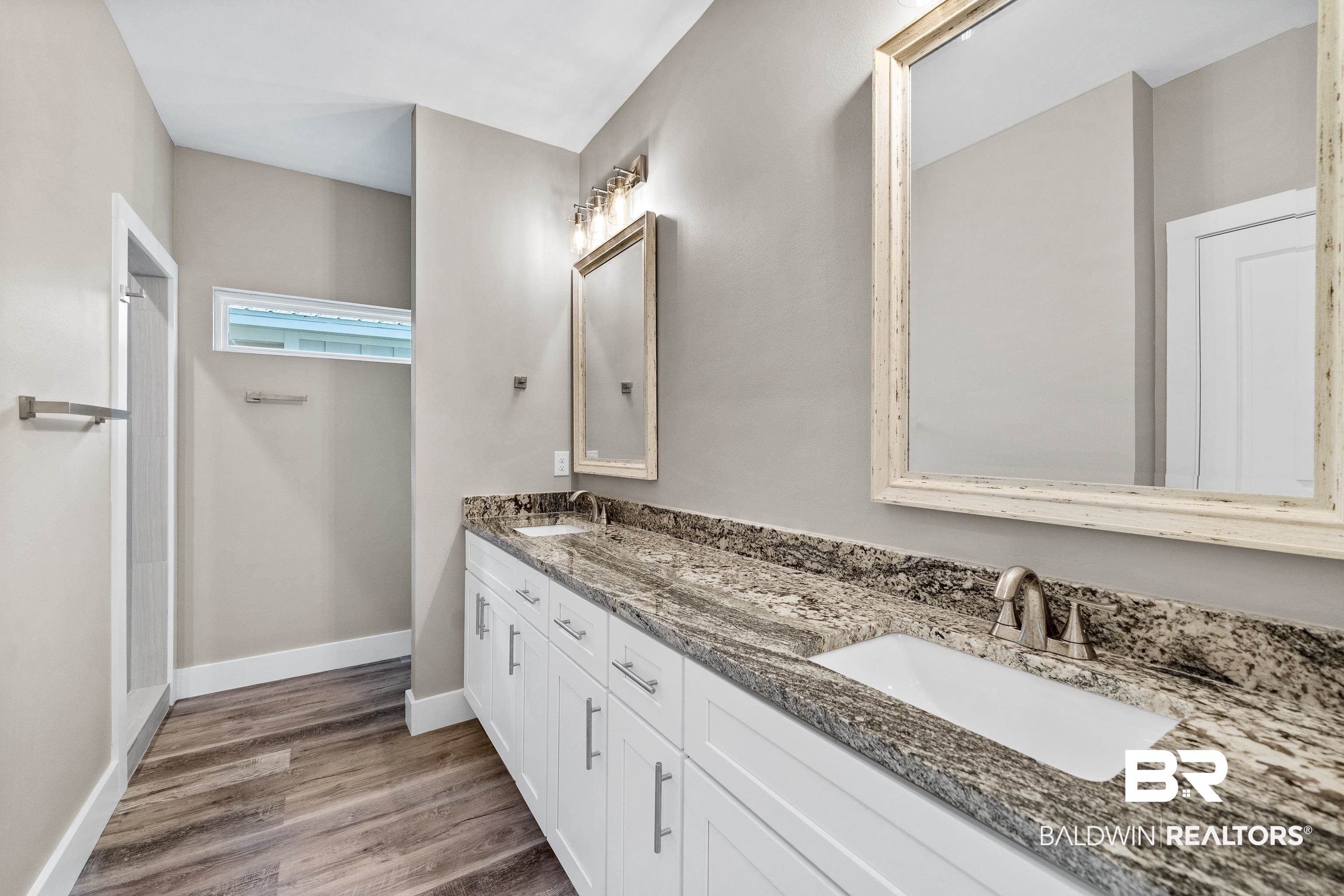 Bathroom with a long double-sink vanity, mottled stone countertop, white cabinets, and large framed mirrors.