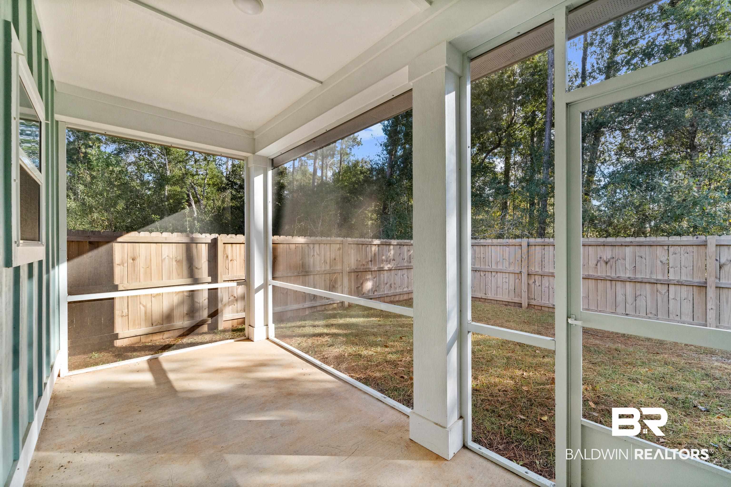 Empty screened porch overlooking a fenced backyard with mature trees.