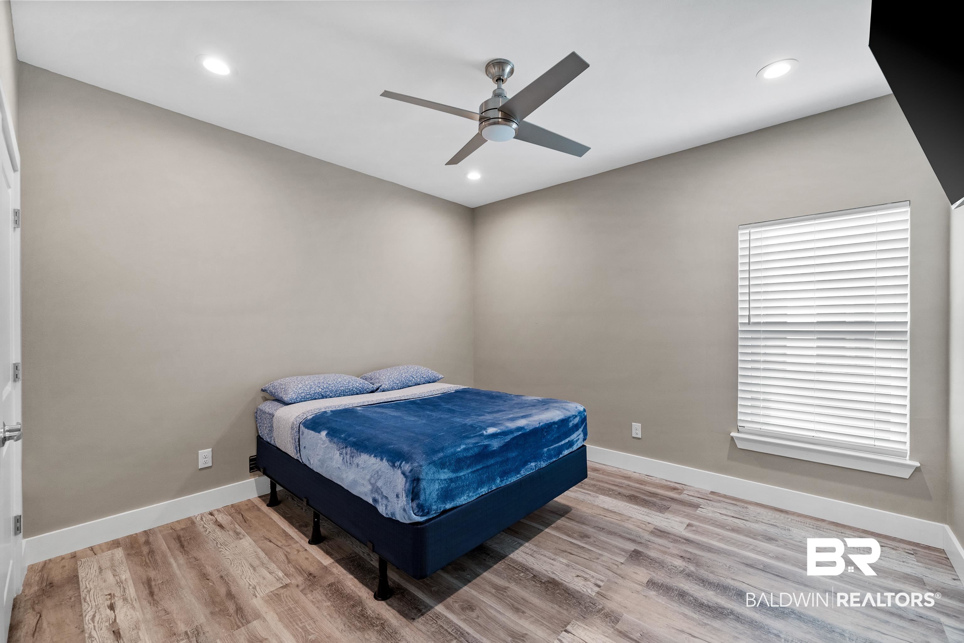 Bedroom with a blue bed, wood-look flooring, and a ceiling fan.