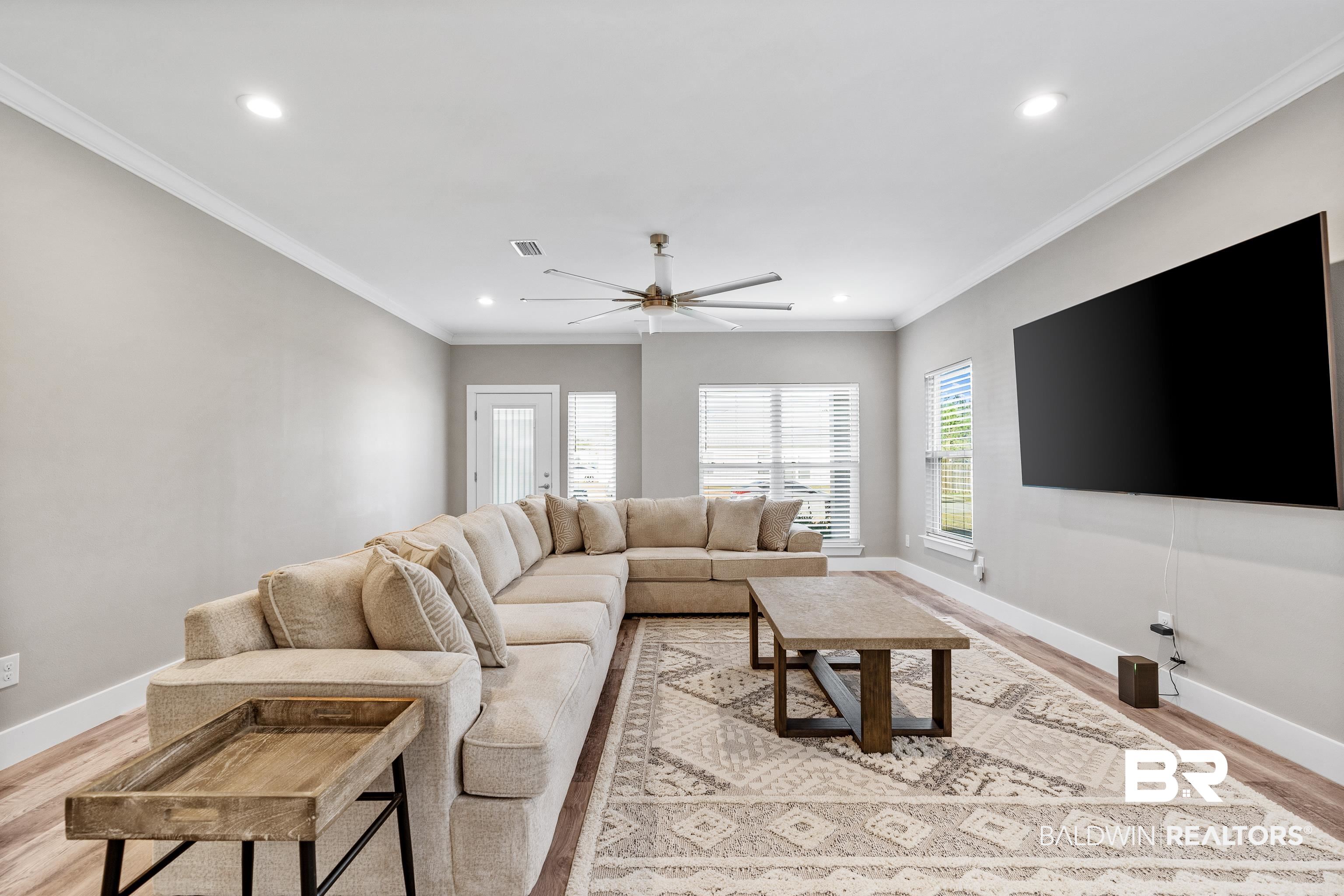Living room with a beige sectional, patterned rug, wall-mounted television, and large windows.