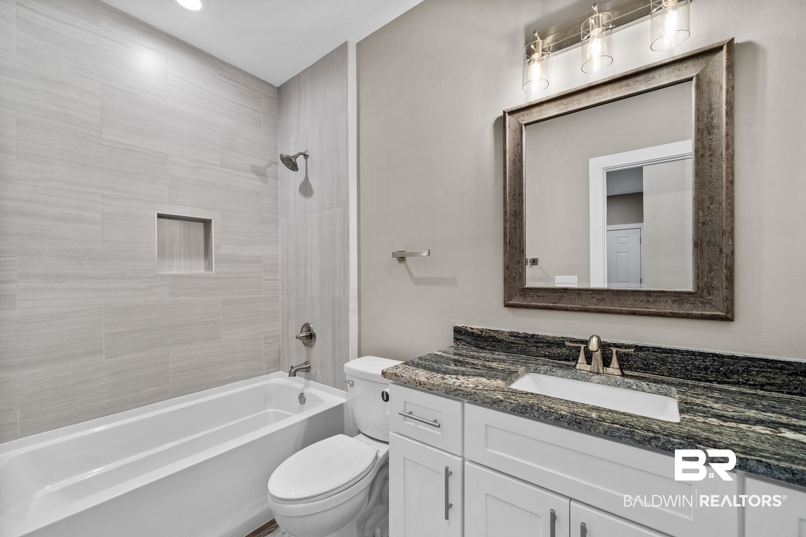 Bathroom with a white bathtub, tiled shower wall, and white vanity topped with dark granite.