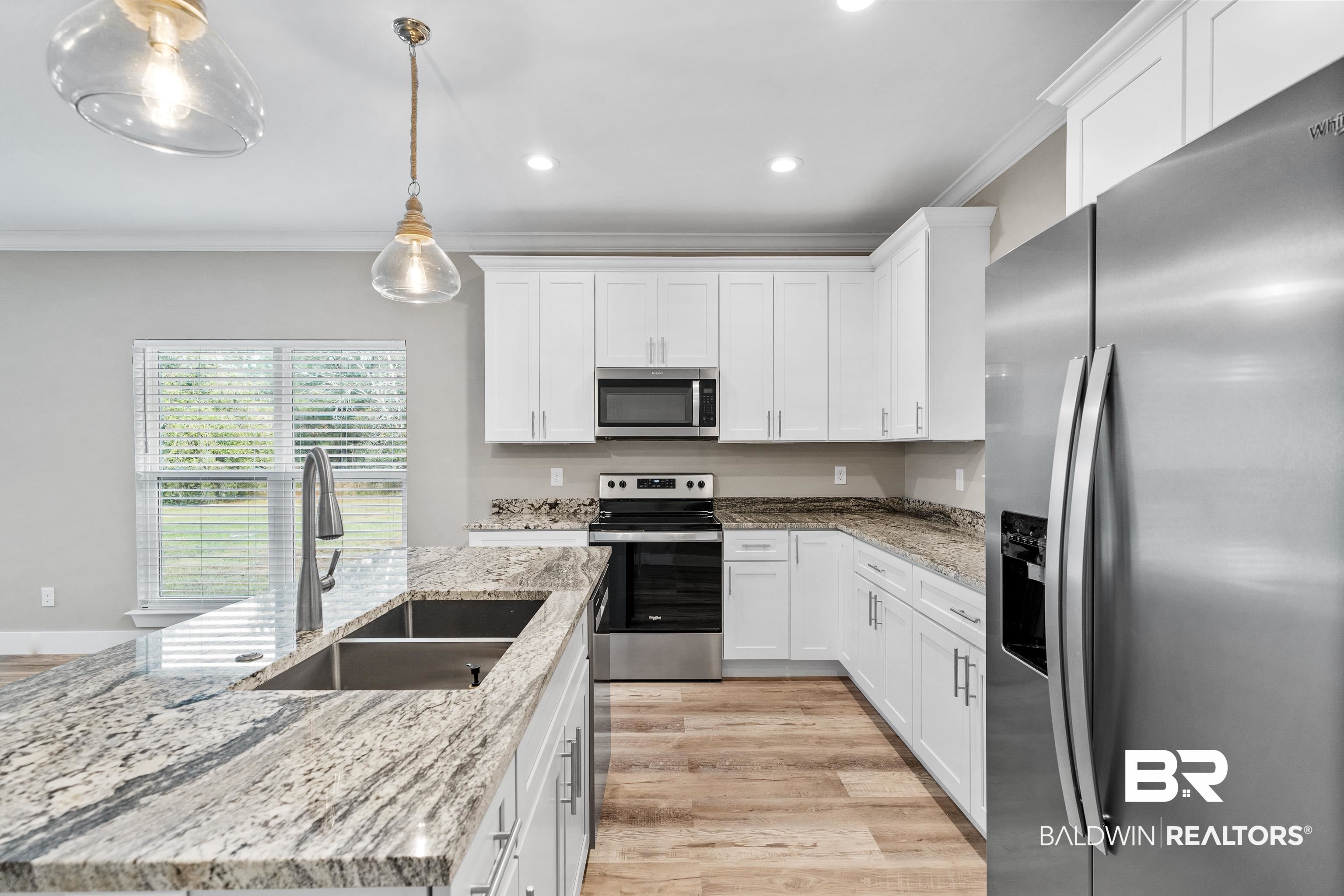 Kitchen with white cabinets, granite countertops, a large sink island, and stainless steel appliances.