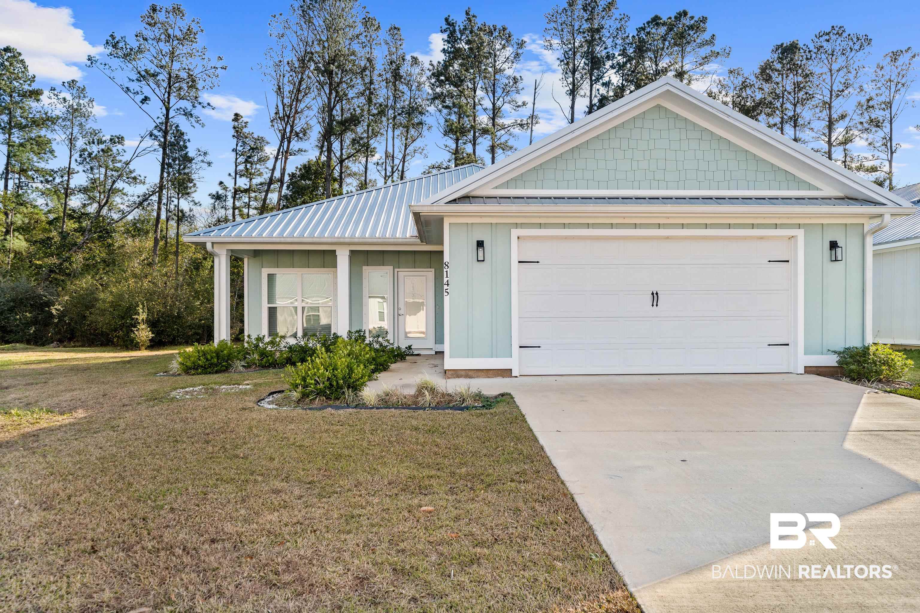 Pale mint-green home with a metal roof, white garage, and landscaped front yard.