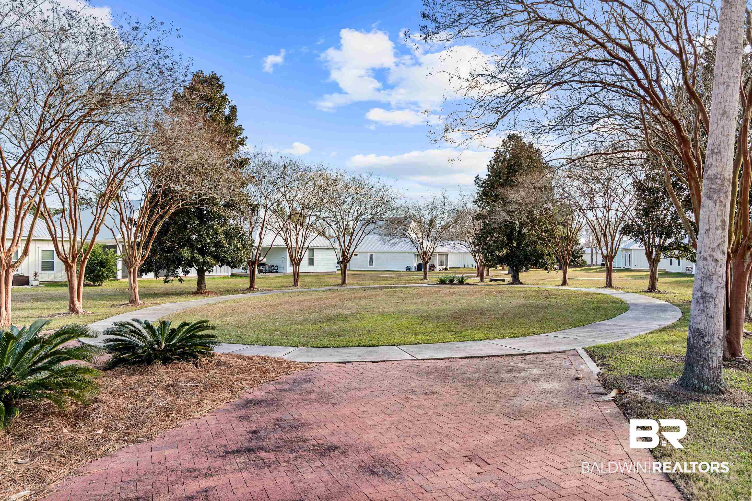 Residential courtyard with a curved walkway, grassy lawn, mature trees, and low white homes.