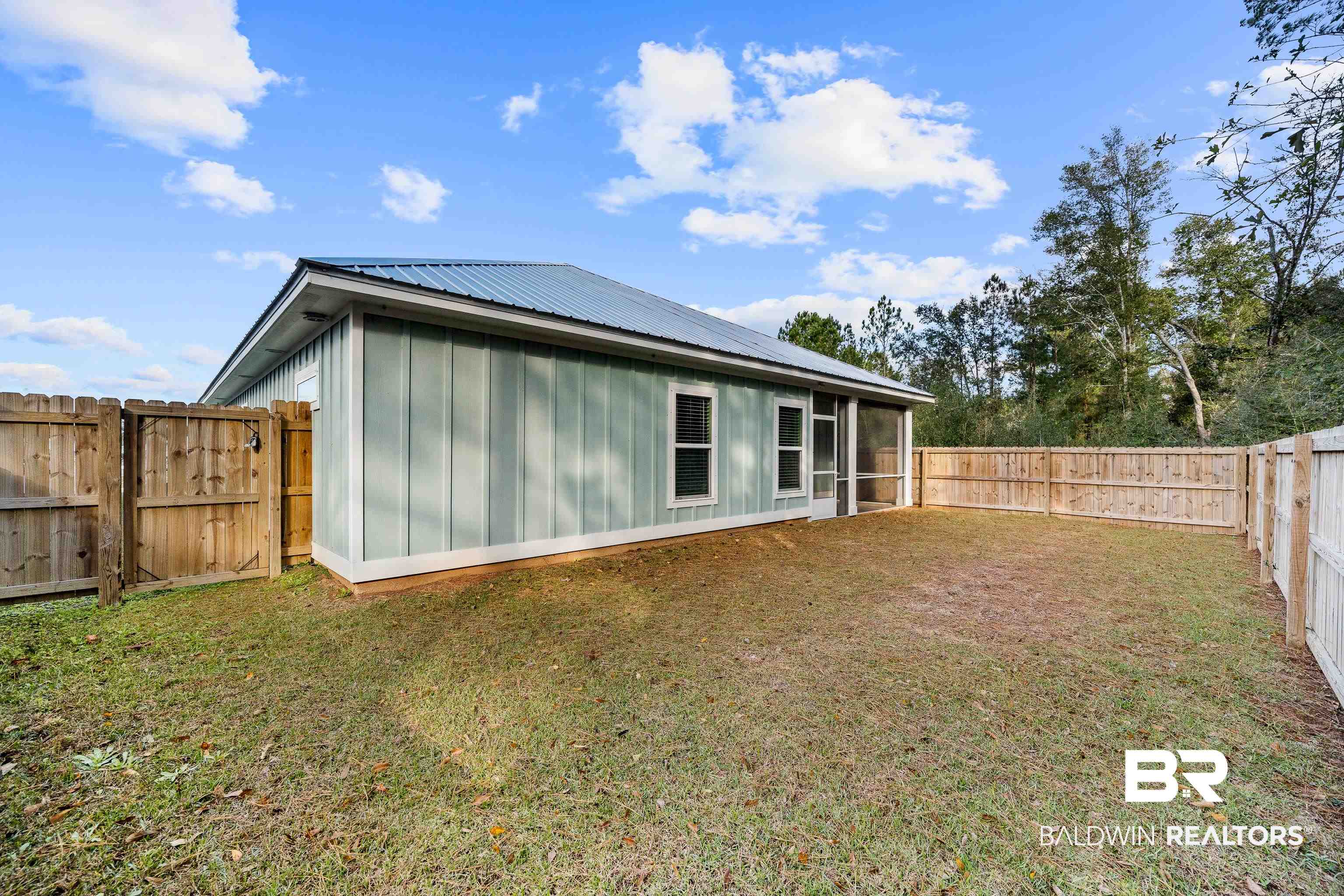Pale green home with a screened porch behind a spacious fenced backyard.