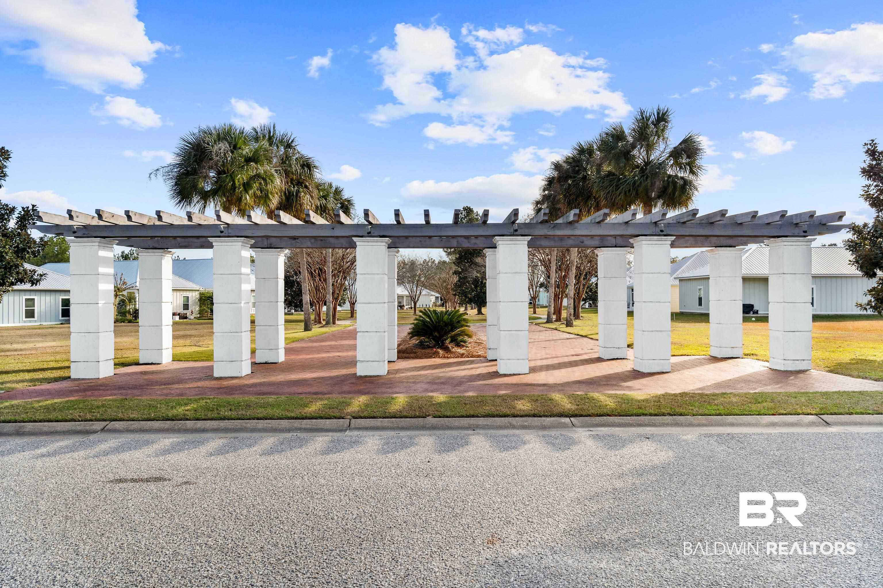 White-columned pergola over a brick walkway, with palm trees and homes in the background.
