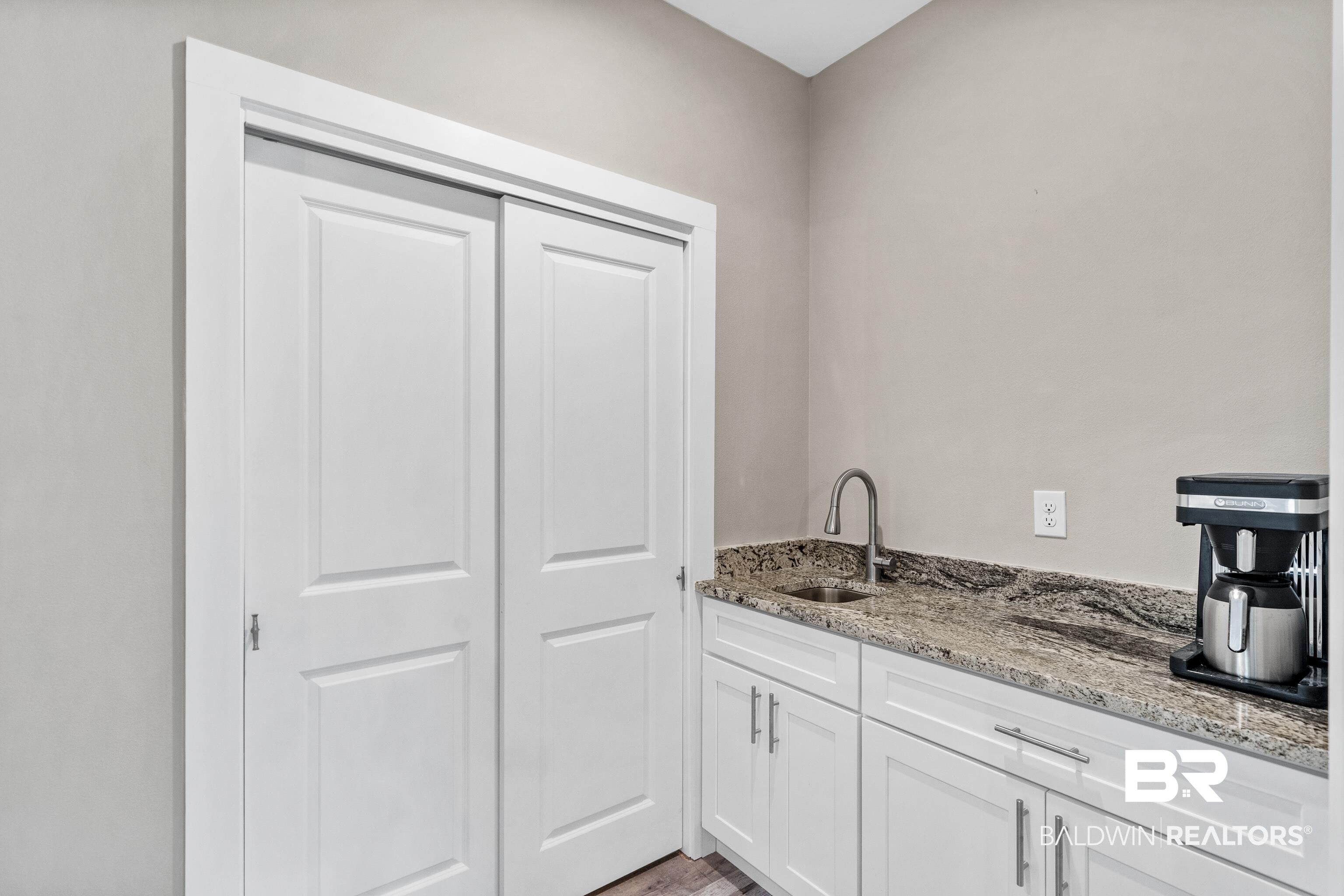 Kitchen coffee bar with granite counter, small sink, white cabinetry, and drip coffee maker.