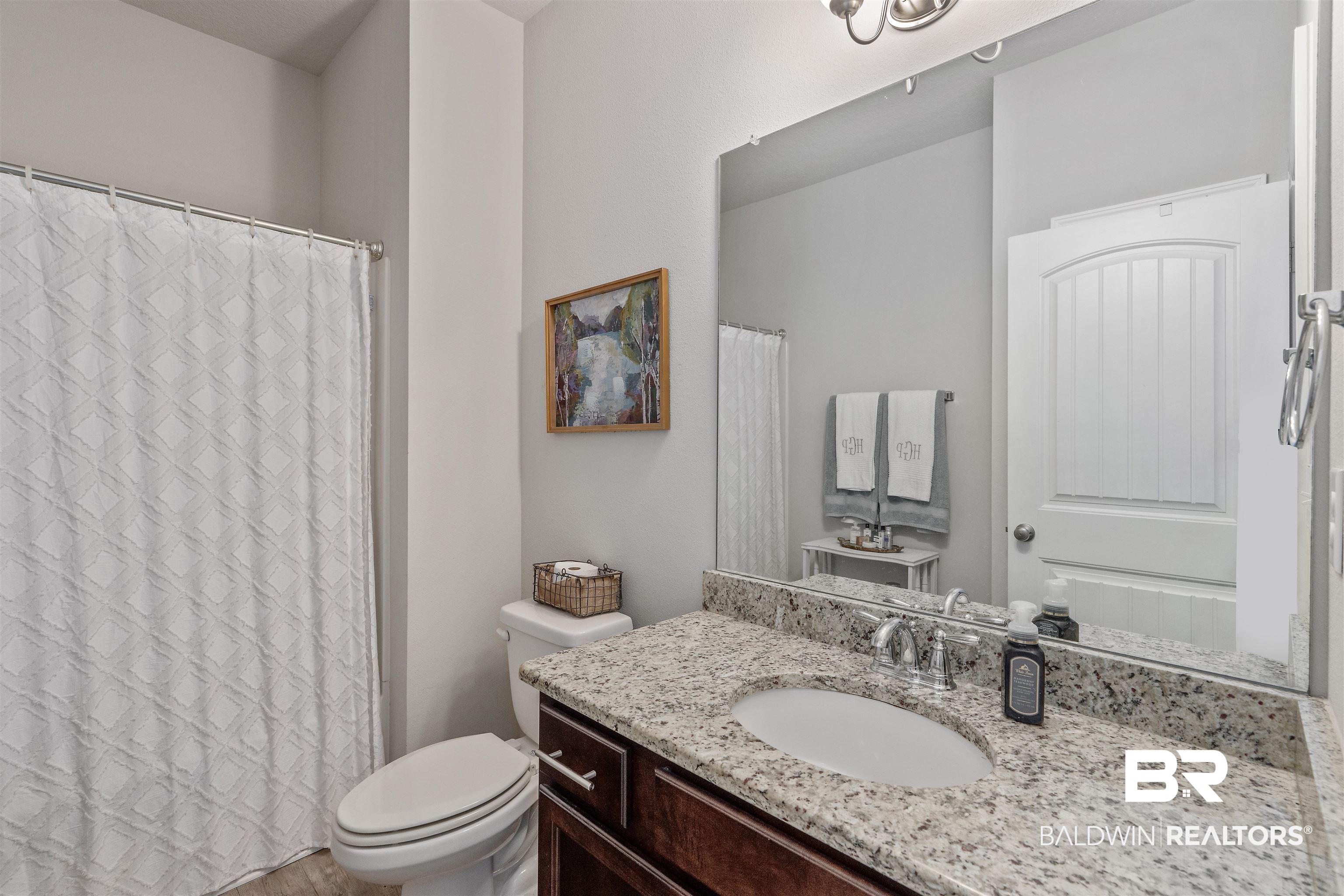 Bathroom with a speckled granite vanity, oval sink, and patterned white shower curtain.