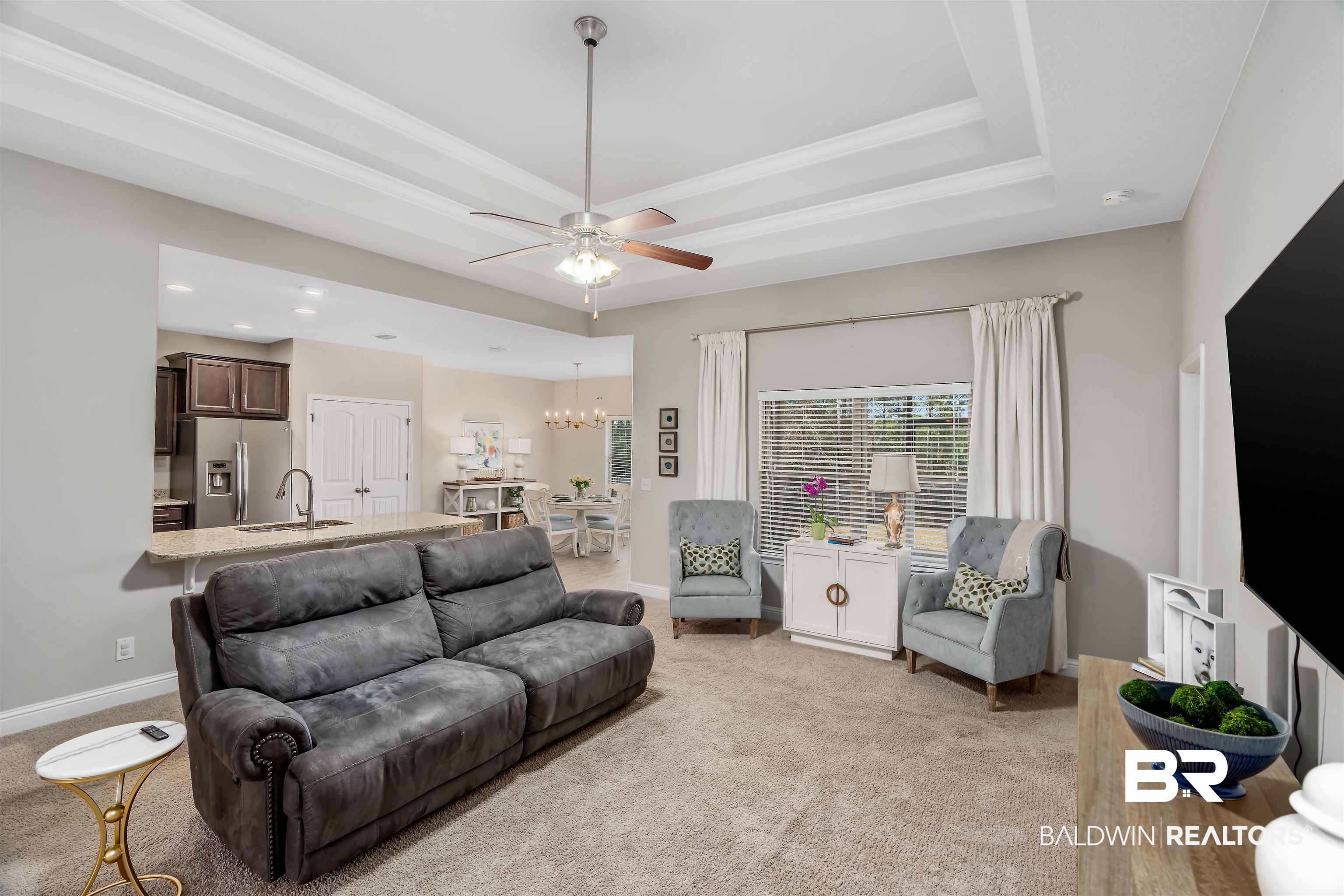 Living room with a gray leather sofa, pale blue armchairs, and an open view into the kitchen and dining area.