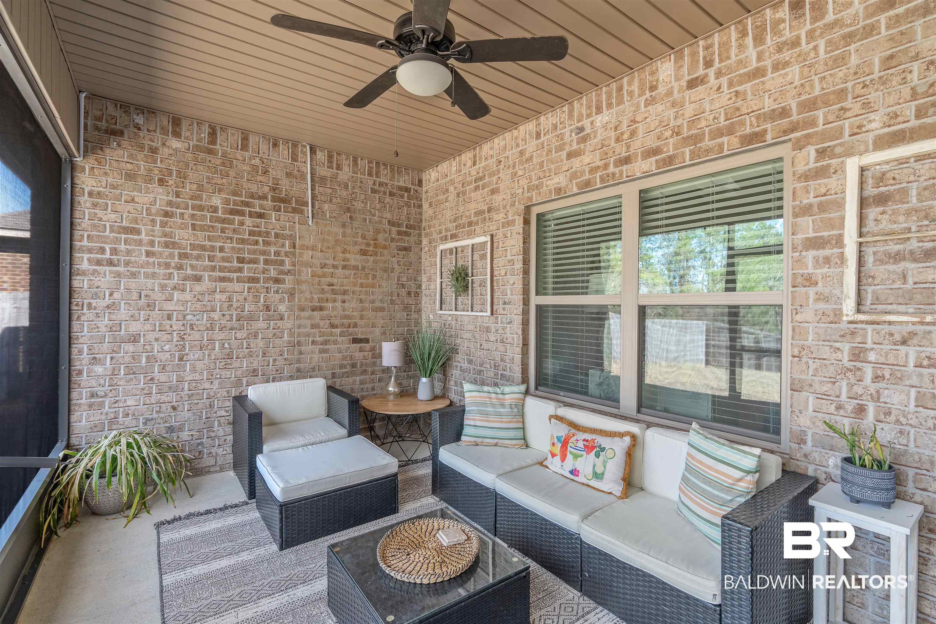 Covered patio with wicker seating, brick walls, and a ceiling fan.