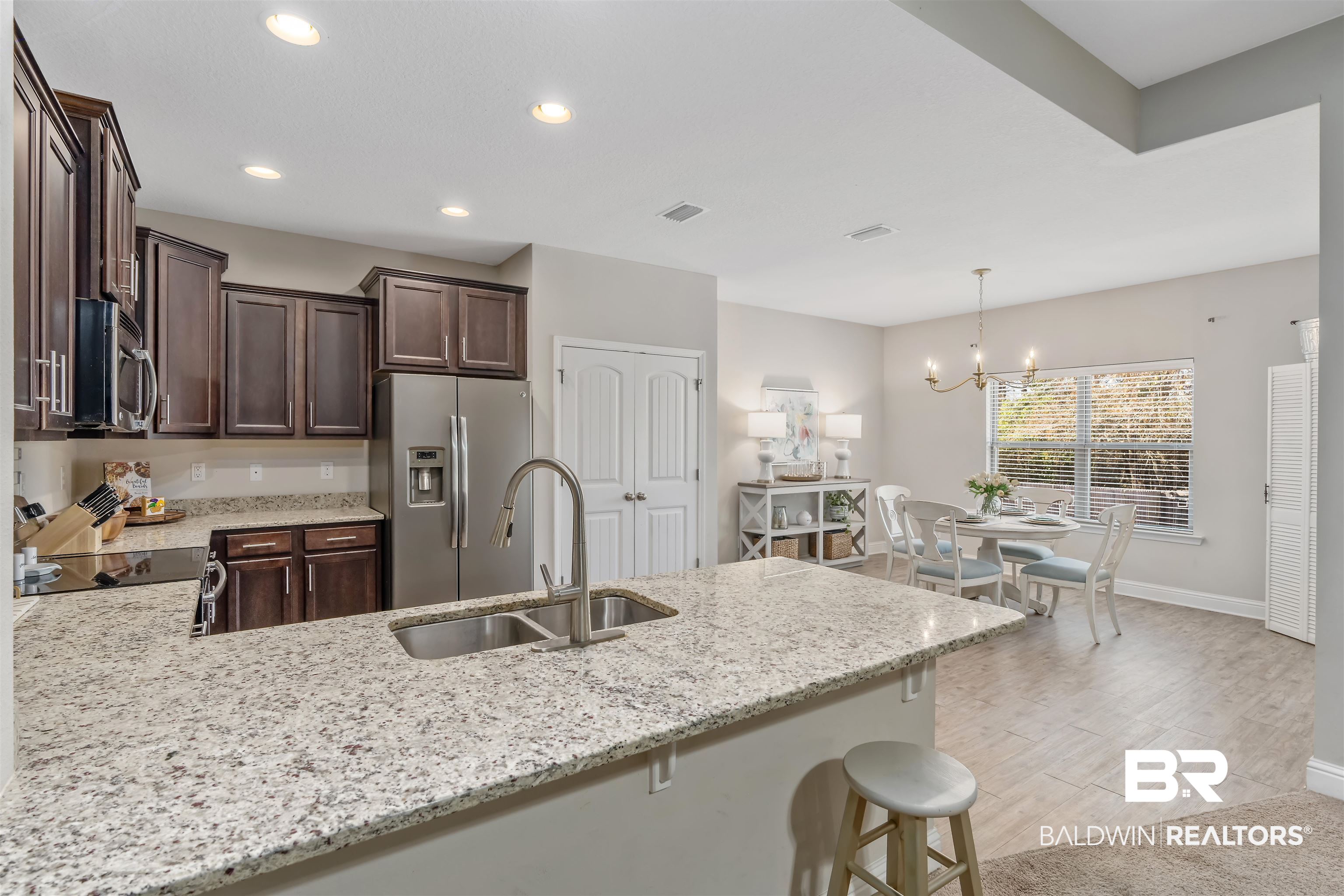 Kitchen with granite island and double sink, dark wood cabinets, and an adjoining dining area.