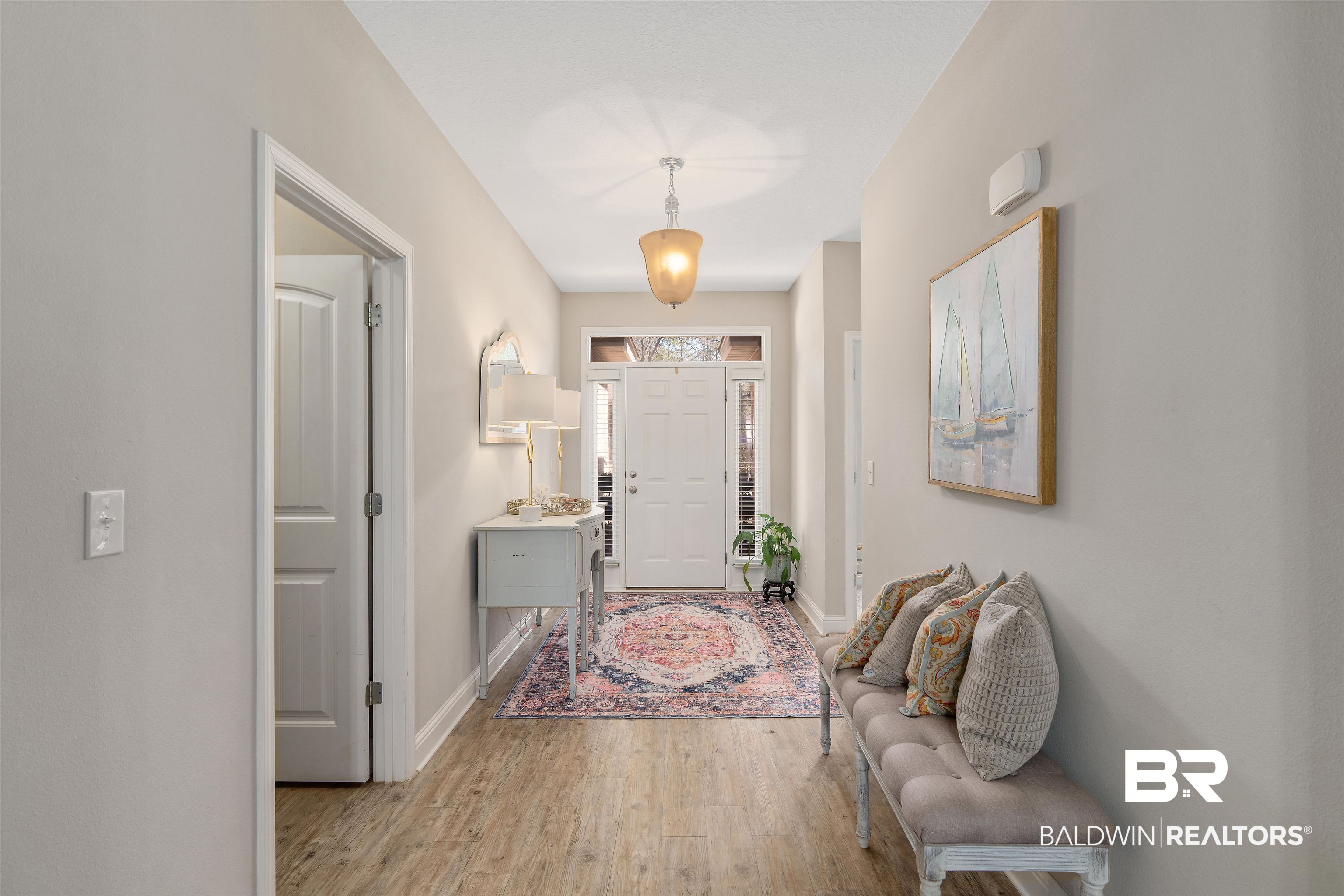 Bright entry hall with a patterned runner, pale console table, cushioned bench, and white front door.