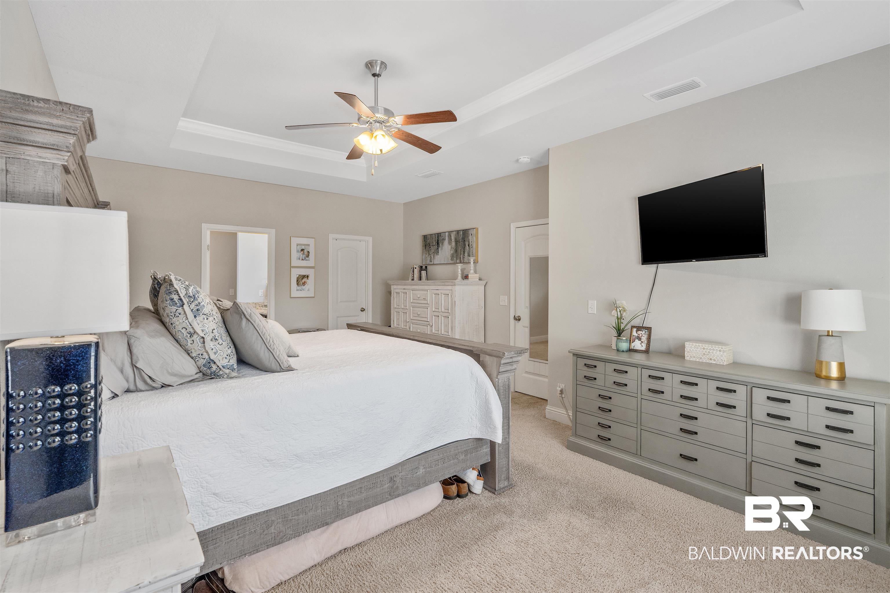 Furnished bedroom with a gray bed, white bedding, long dresser, and wall-mounted television.