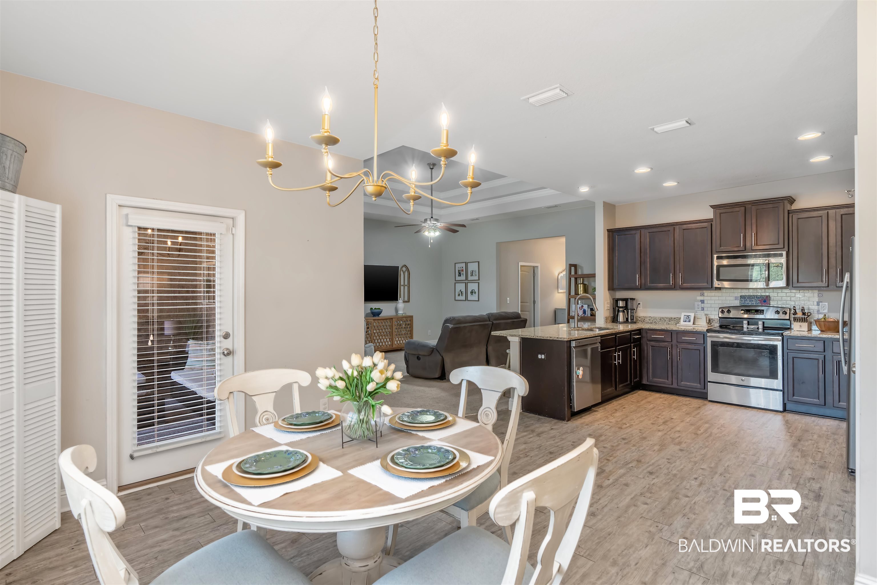 Open-plan dining room and kitchen with a set table, dark cabinets, stainless appliances, and a large island.