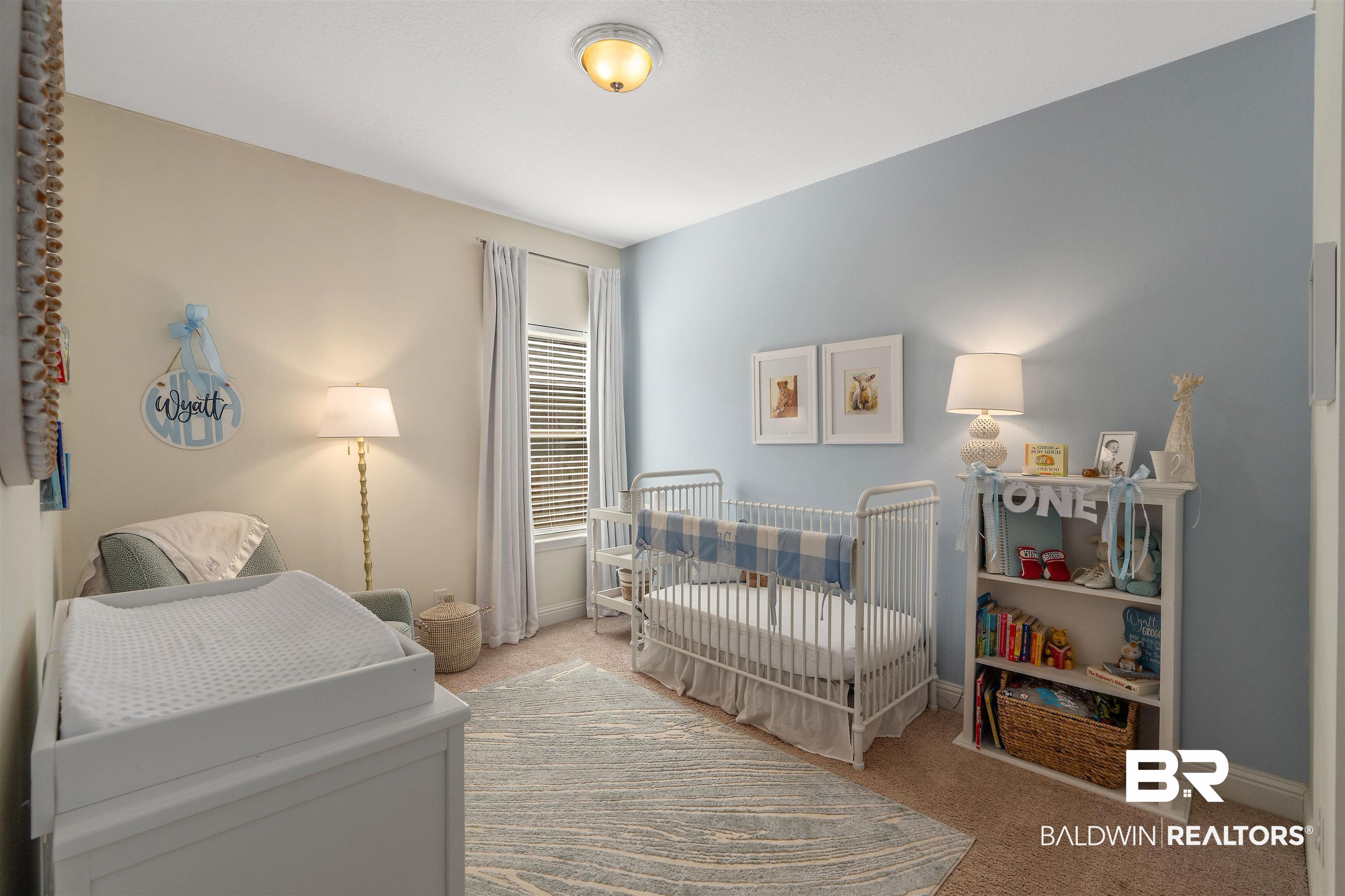 Nursery with a white crib, blue accent wall, changing table, and Wyatt wall decor.