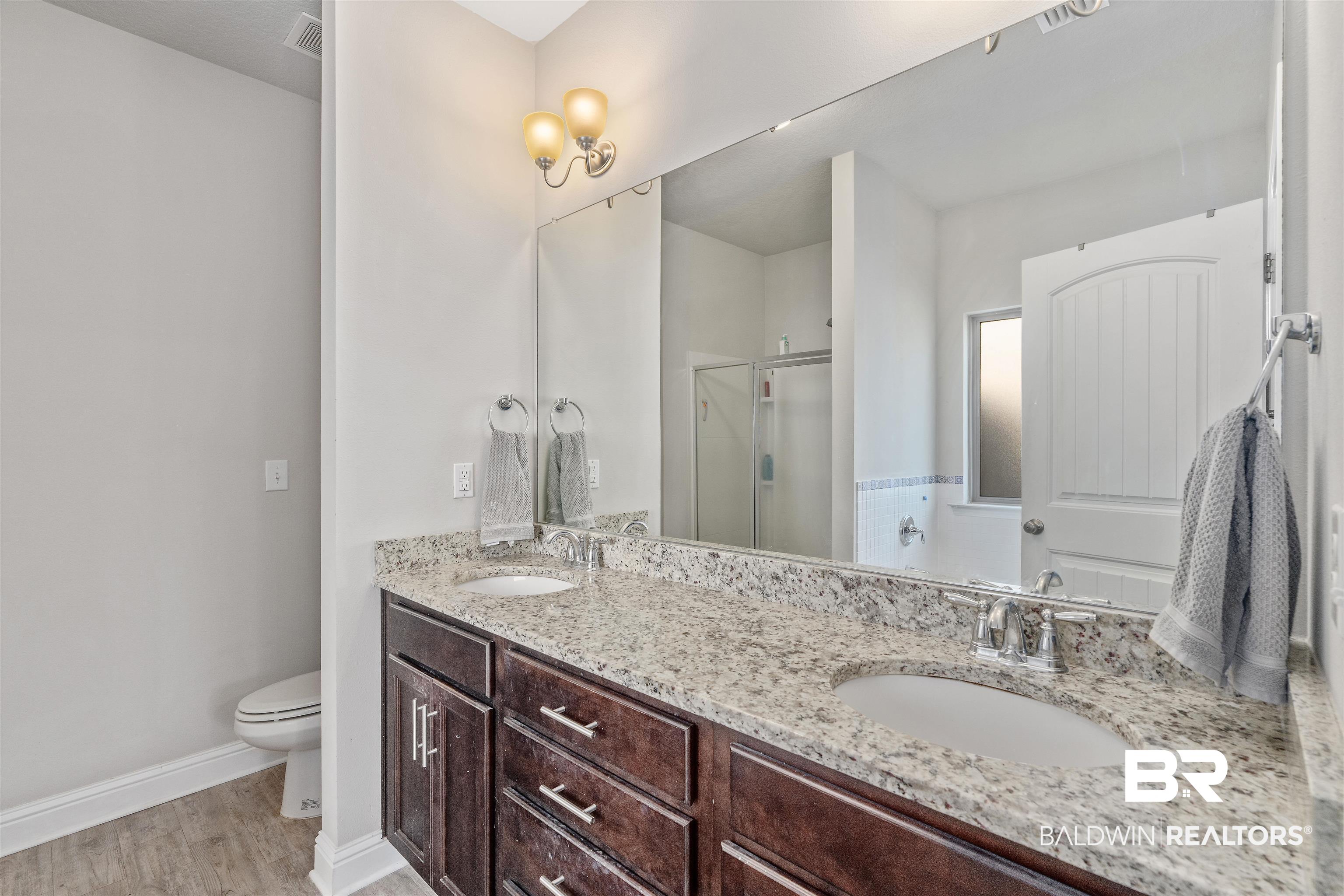 Bathroom with a double-sink granite vanity, dark wood cabinets, and glass-enclosed shower.