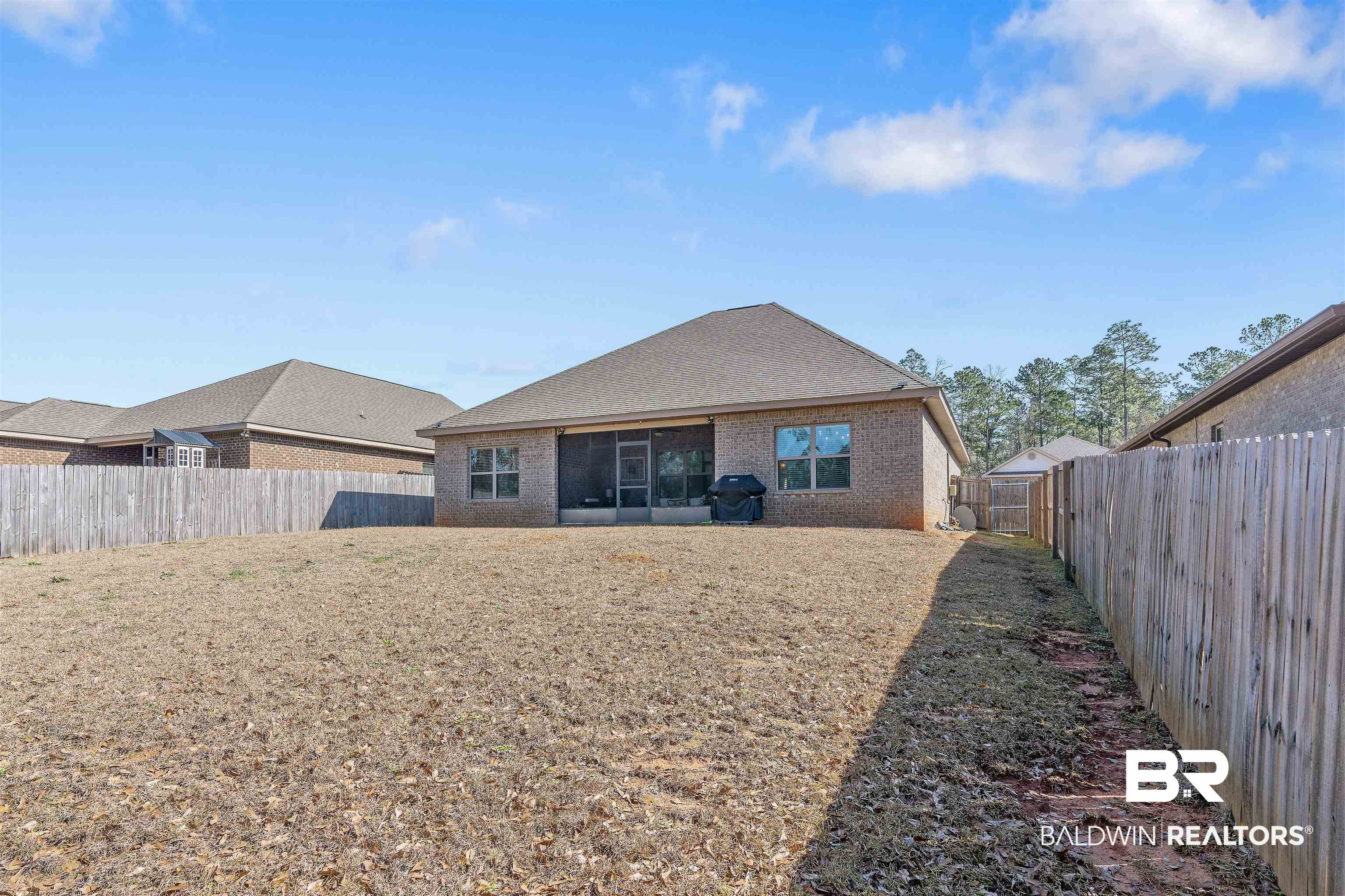 Brick home’s rear exterior and fenced backyard with a broad lawn and sliding glass doors.
