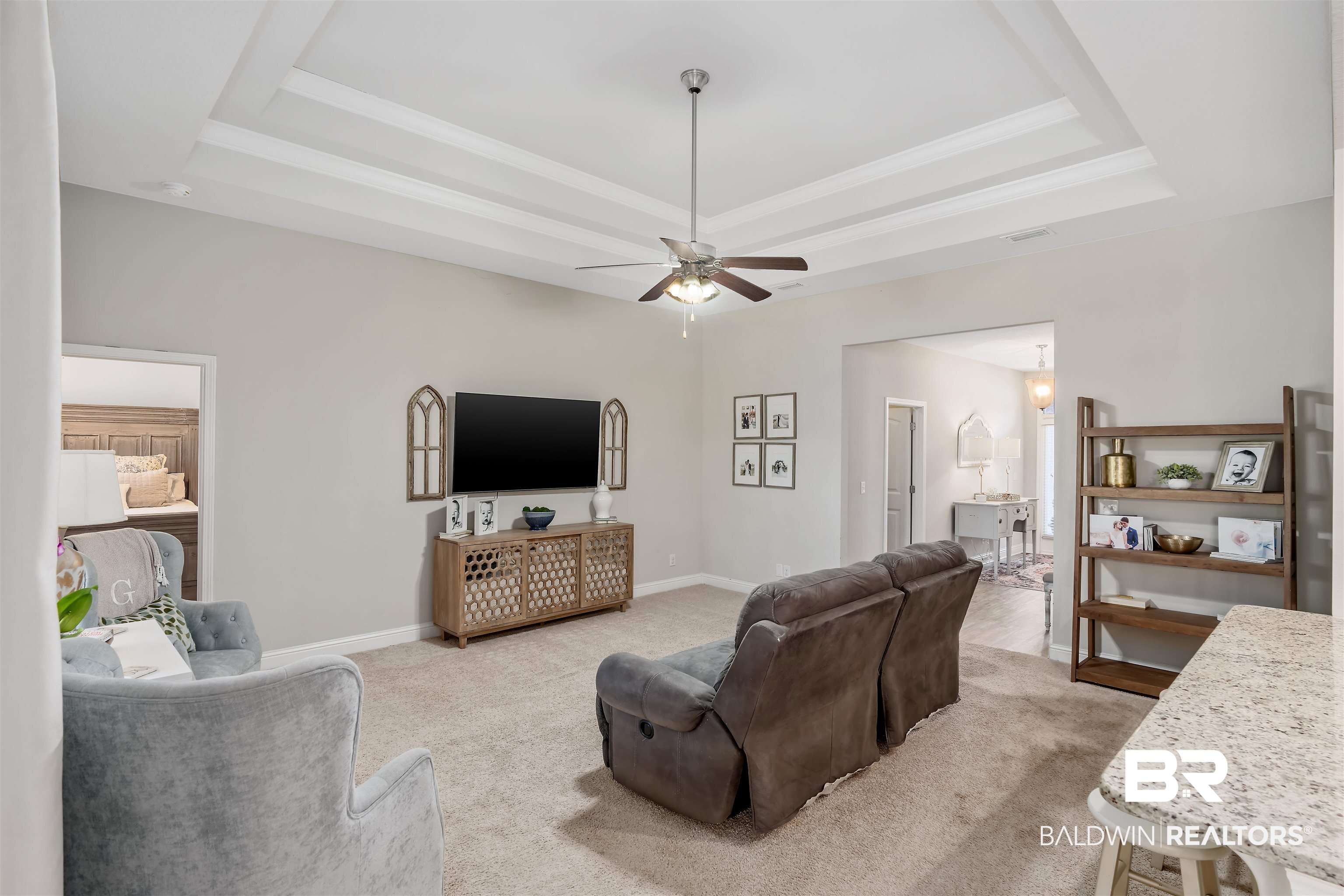 Living room with tray ceiling, brown recliners, gray armchair, and wall-mounted TV.