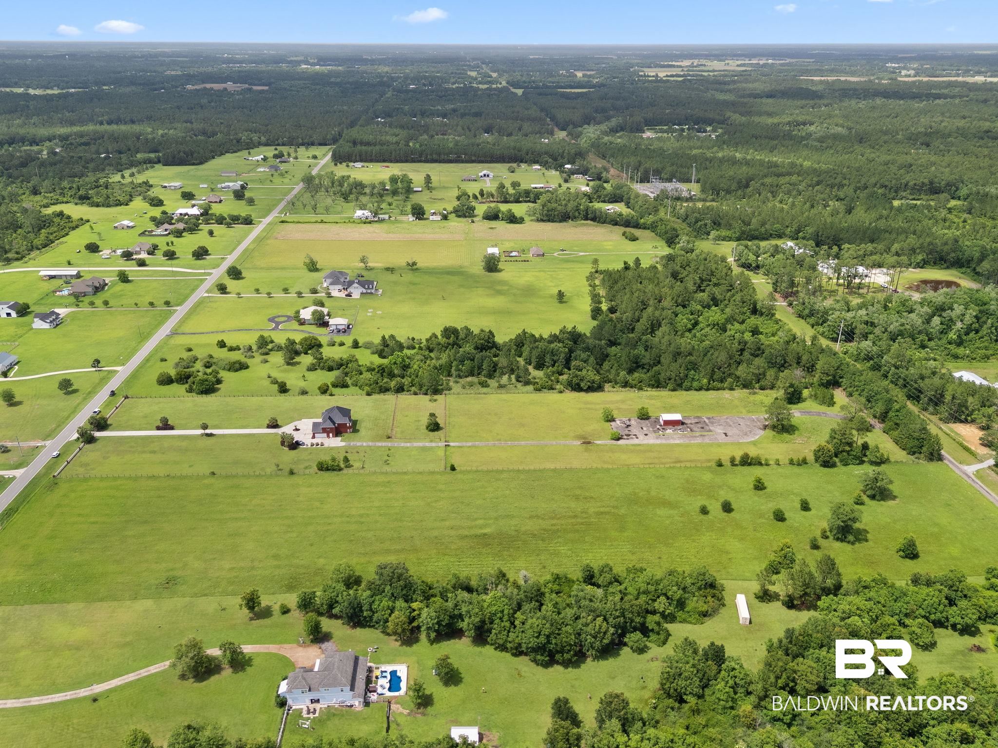 Aerial view of grassy acreage, scattered homes, and woods around 9790 Stucki Road.