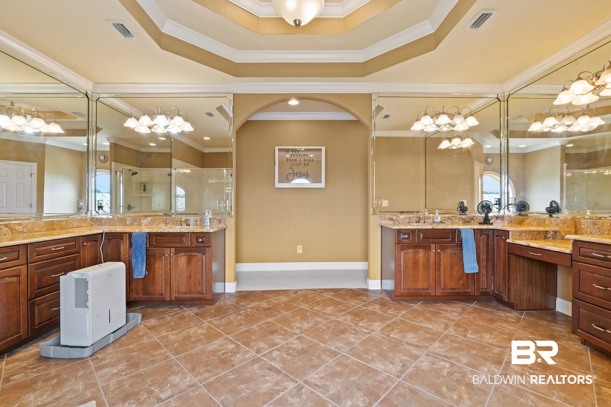 Spacious bathroom with mirrored double vanities, dark wood cabinets, amber countertops, and a tiled floor.