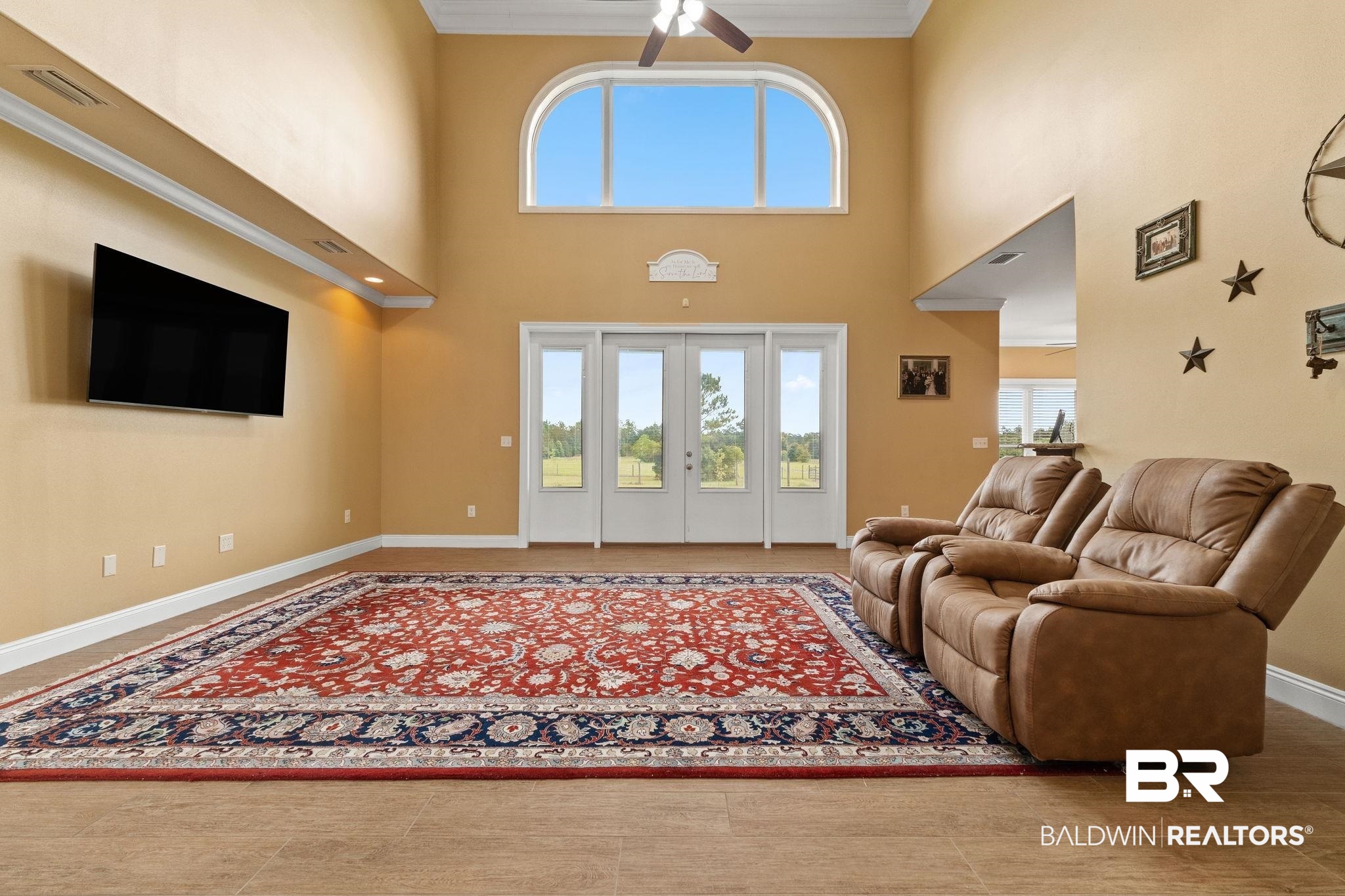 Vaulted living room with tan recliners, a red patterned rug, and tall arched window.