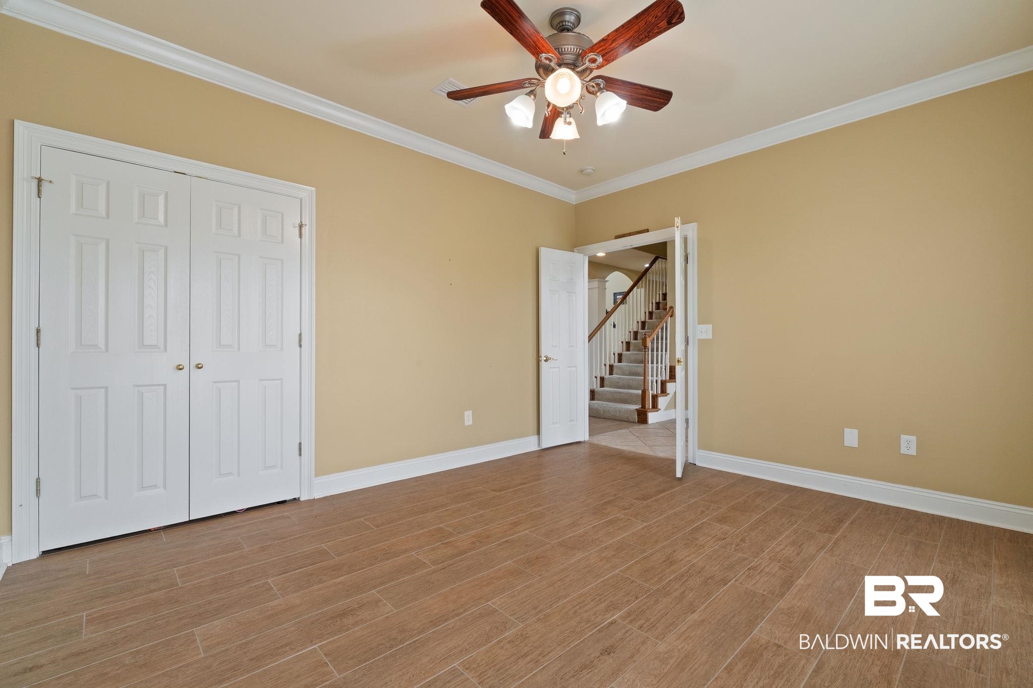 Empty bedroom with wood-look tile flooring, double closet doors, and a ceiling fan.