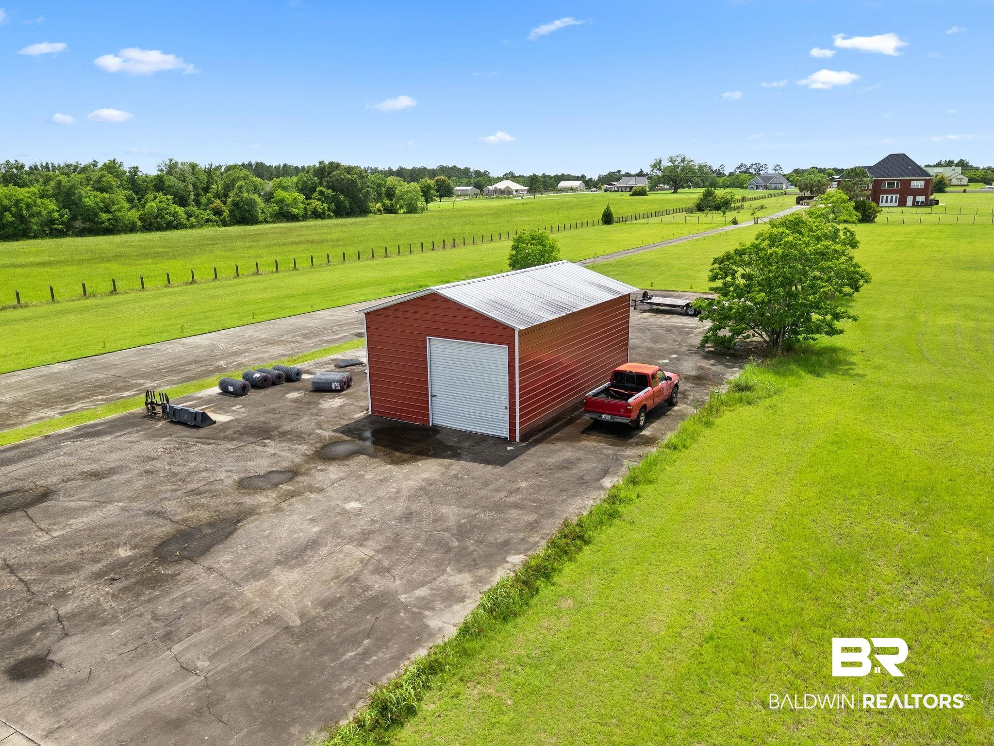 Aerial view of a red metal outbuilding and paved lot surrounded by open grassy land.
