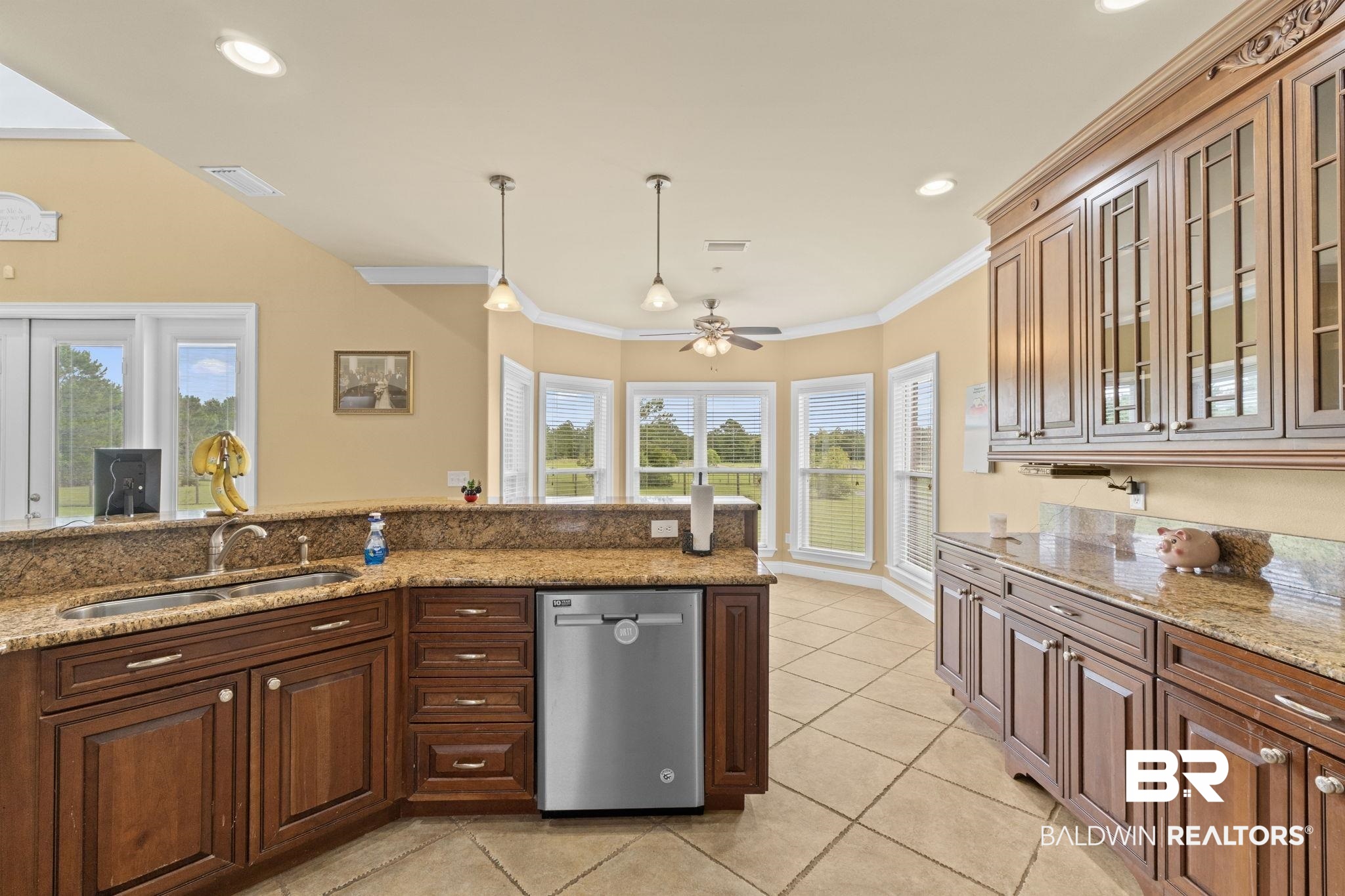 Kitchen with dark wood cabinets, granite counters, a double-basin sink, and windows overlooking greenery.