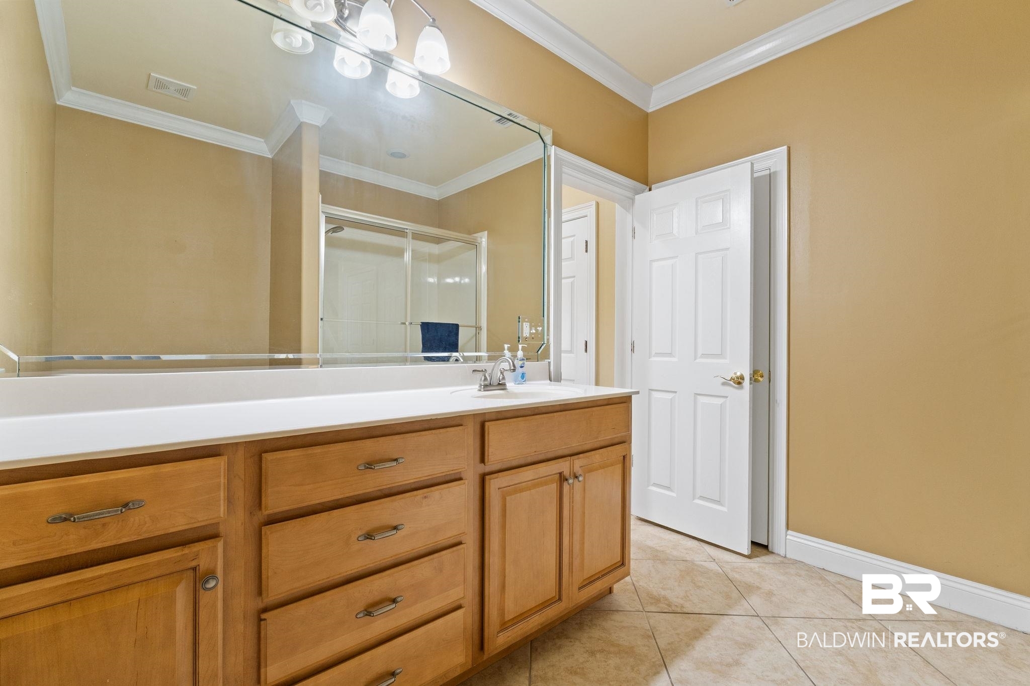 Bathroom with a long wood vanity, white countertop, and large mirror reflecting a glass-enclosed shower.