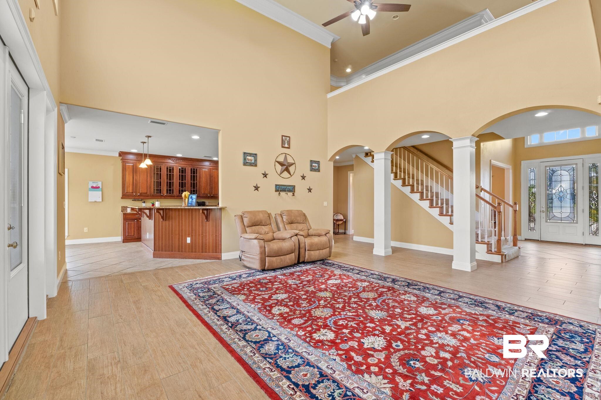 Open living area with vaulted ceiling, red patterned rug, wood bar, and arched staircase.