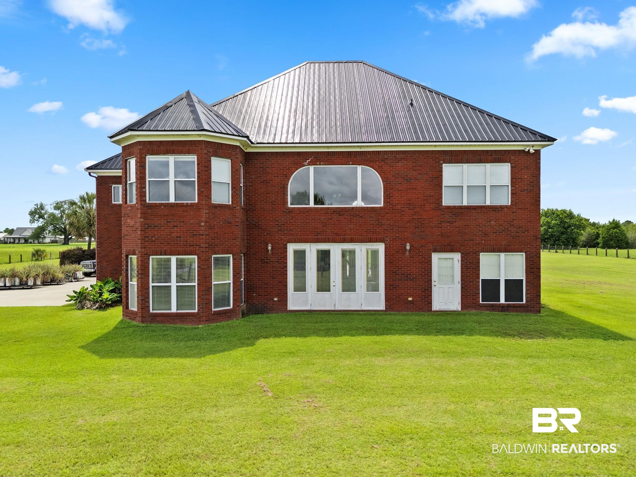 Rear of a two-story red brick house with a metal roof, large windows, and a broad green lawn.