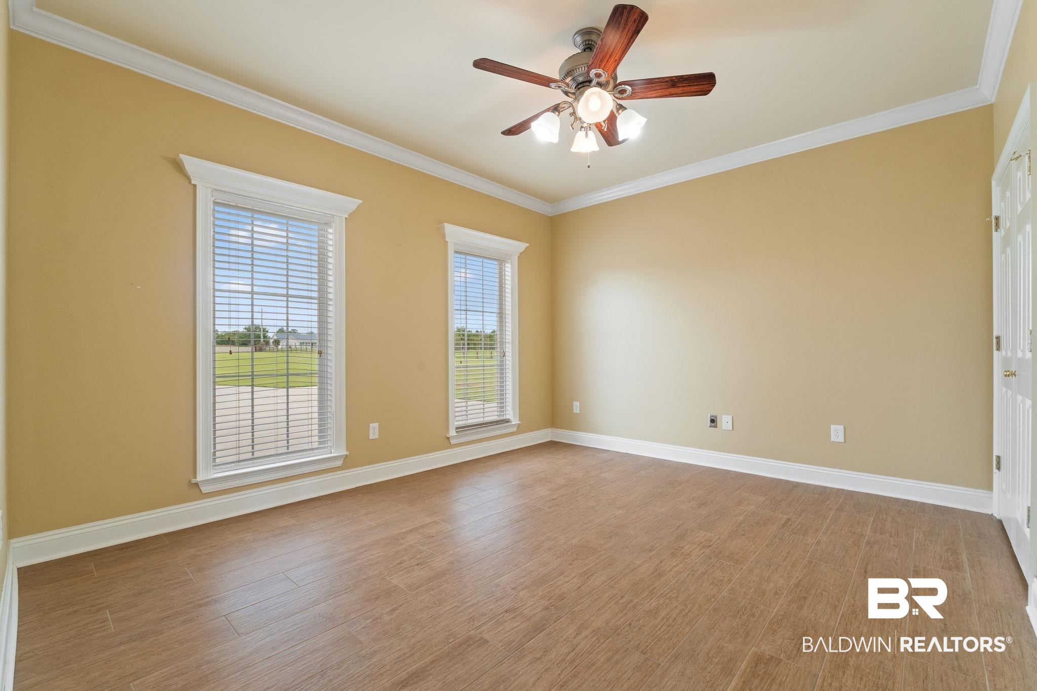 Empty tan room with wood-look tile floors, two windows, and a ceiling fan.
