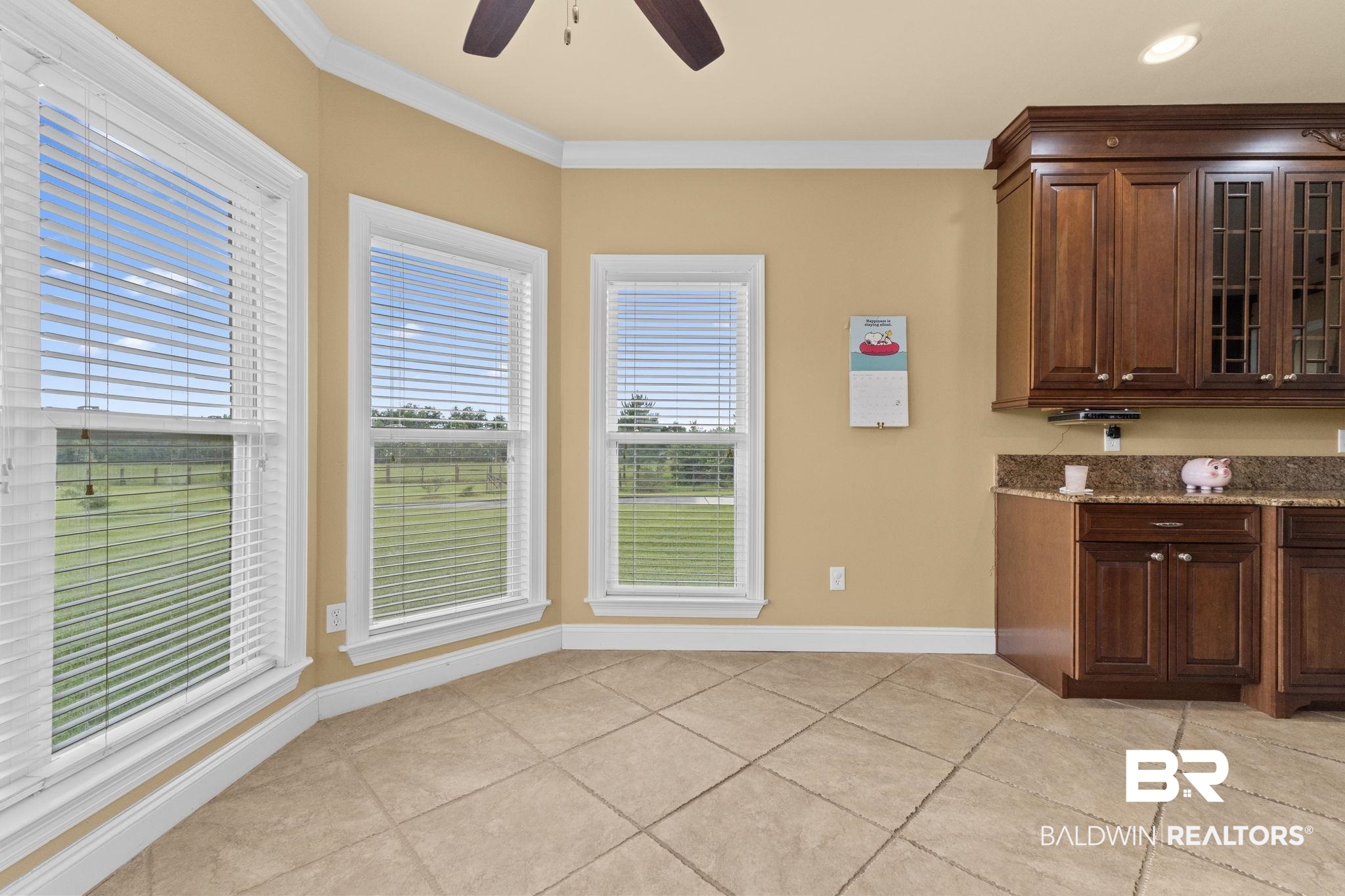 Kitchen with dark wood cabinets, granite counter, beige tile floor, and three large windows.