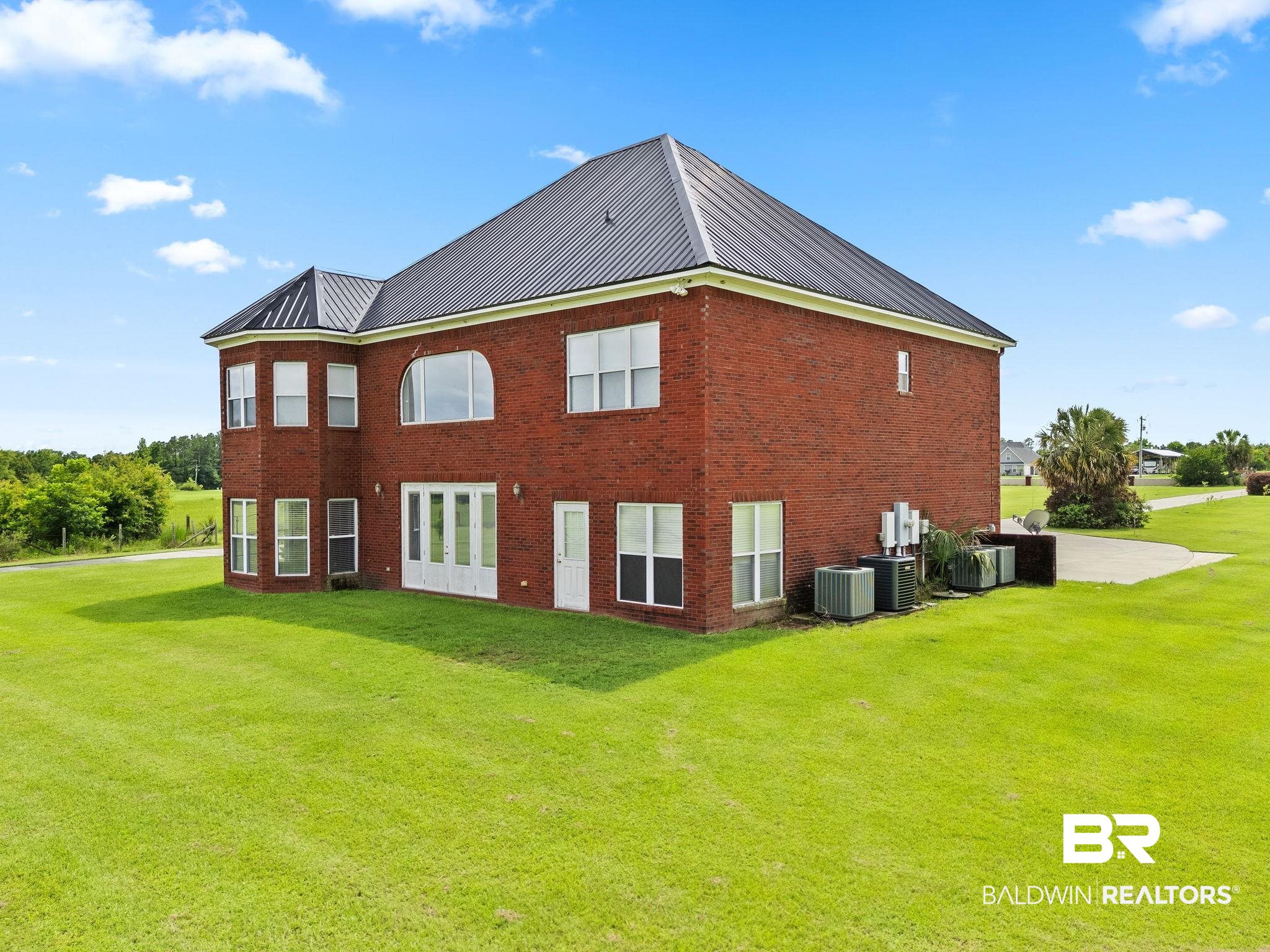 Two-story red-brick home with a steep gray metal roof and broad green lawn.