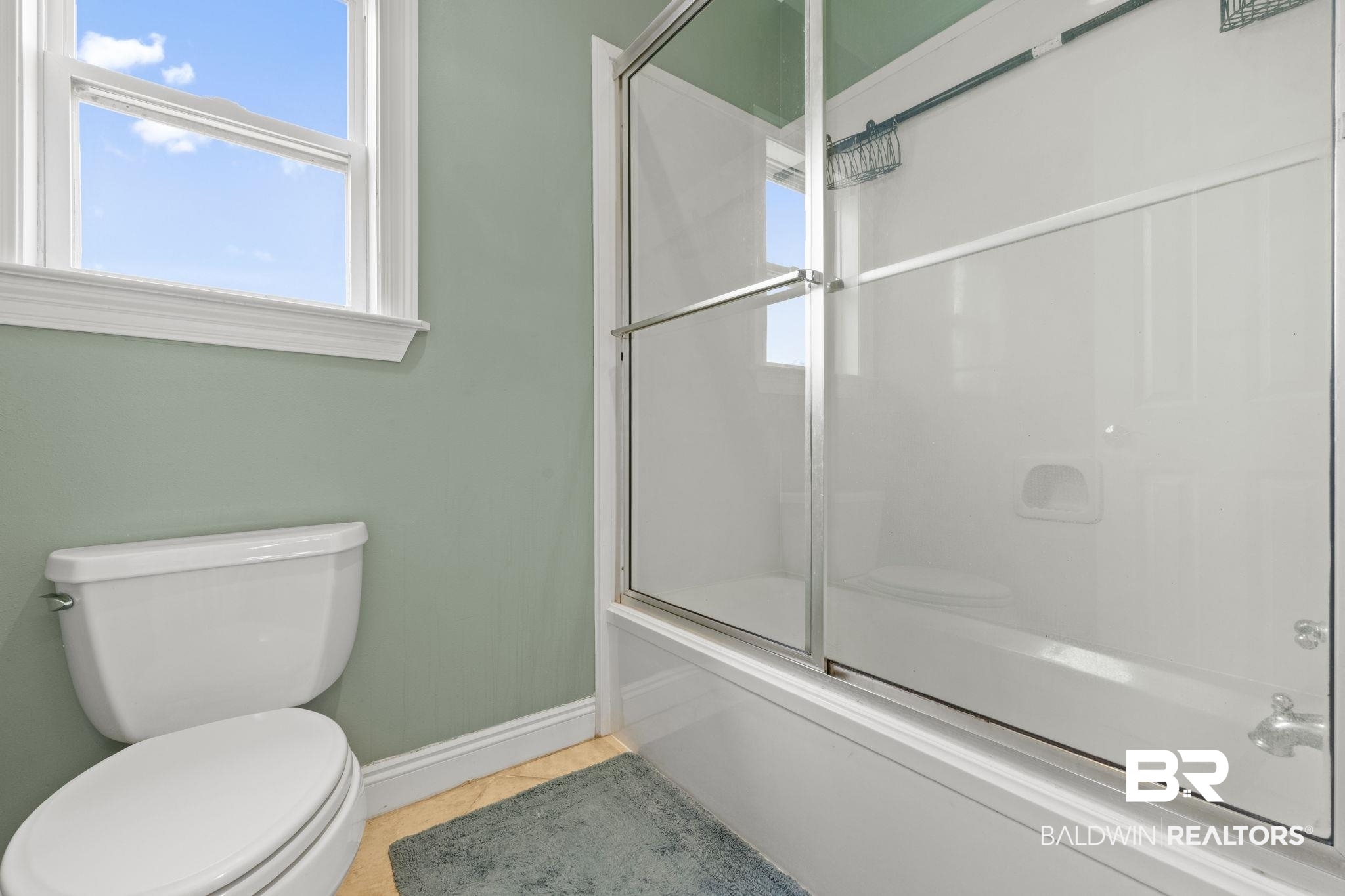 Bathroom with pale green walls, a white toilet, and a tub with sliding glass doors.