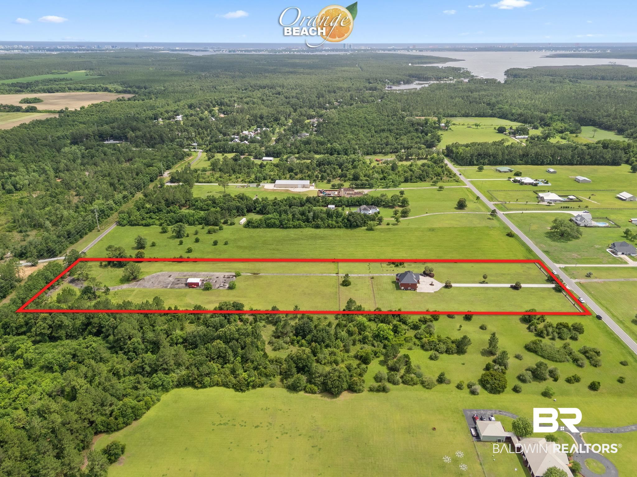 Aerial view of a grassy property outlined in red, with a house and road along one side.