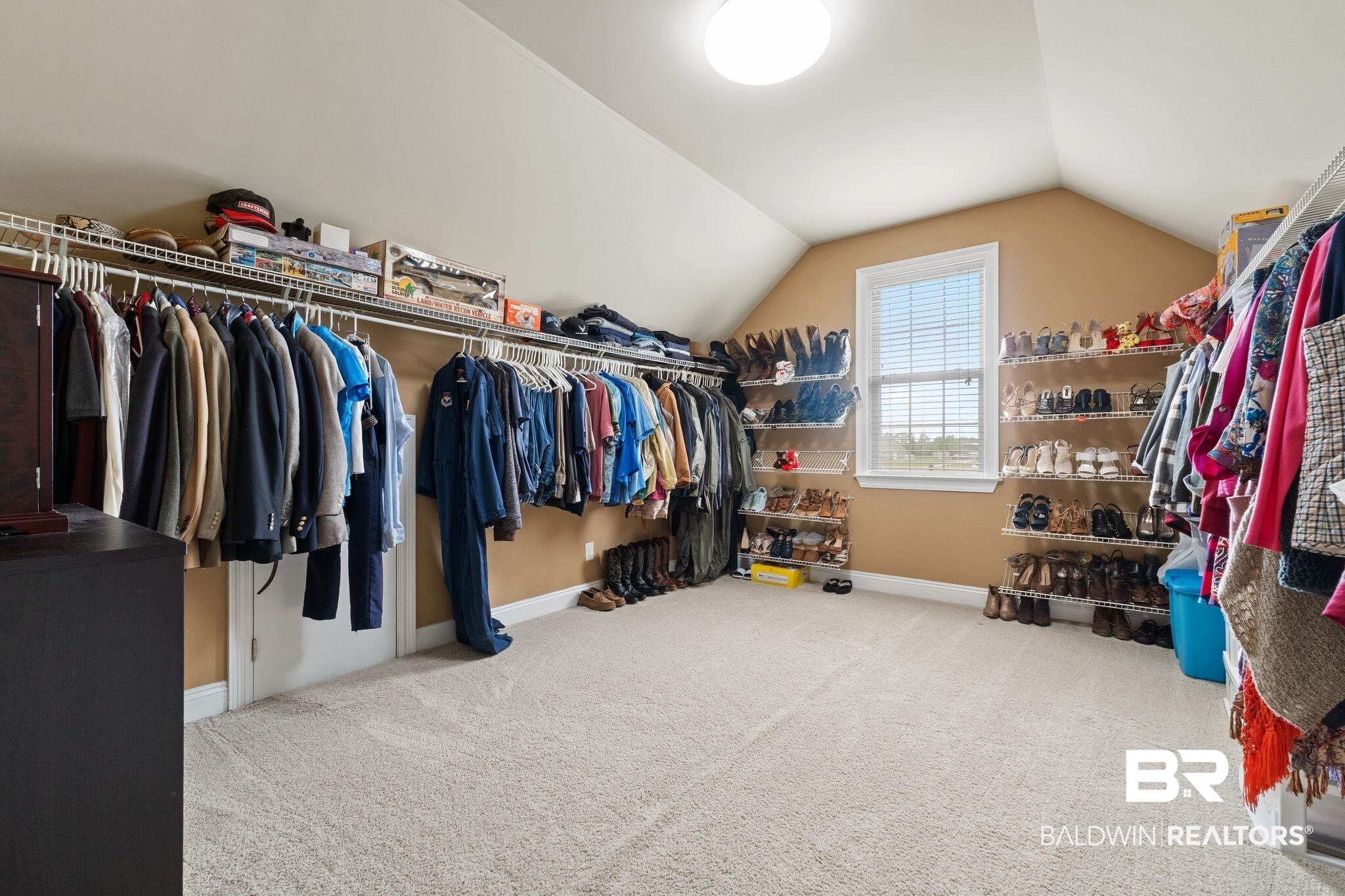 Walk-in closet with vaulted ceiling, extensive clothing racks, shoe shelves, and a window.